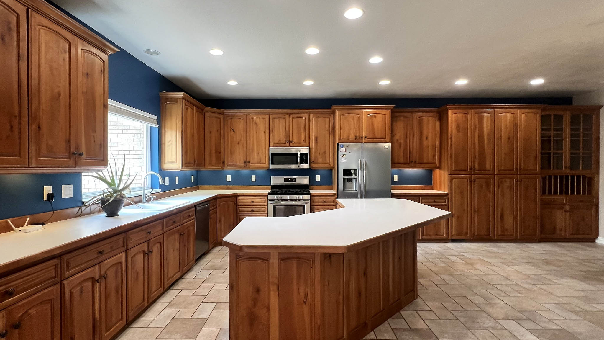 Spacious kitchen featuring extensive wood cabinetry, a central island with white countertop, stainless steel appliances, recessed lighting, and tile flooring
