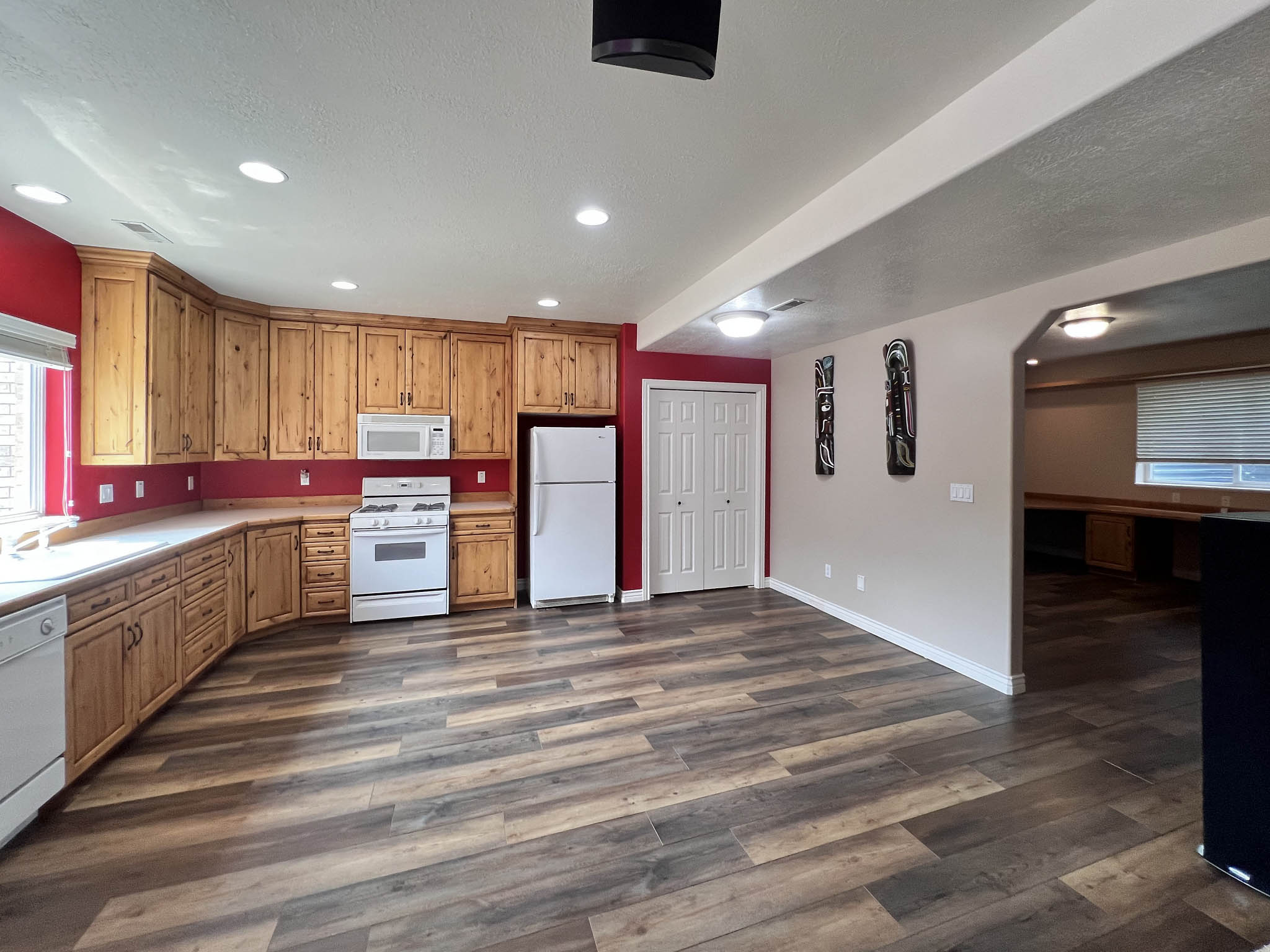 Open-concept kitchen featuring extensive wood cabinetry, white appliances, recessed lighting, wood-finish flooring, and a pantry with bi-fold doors