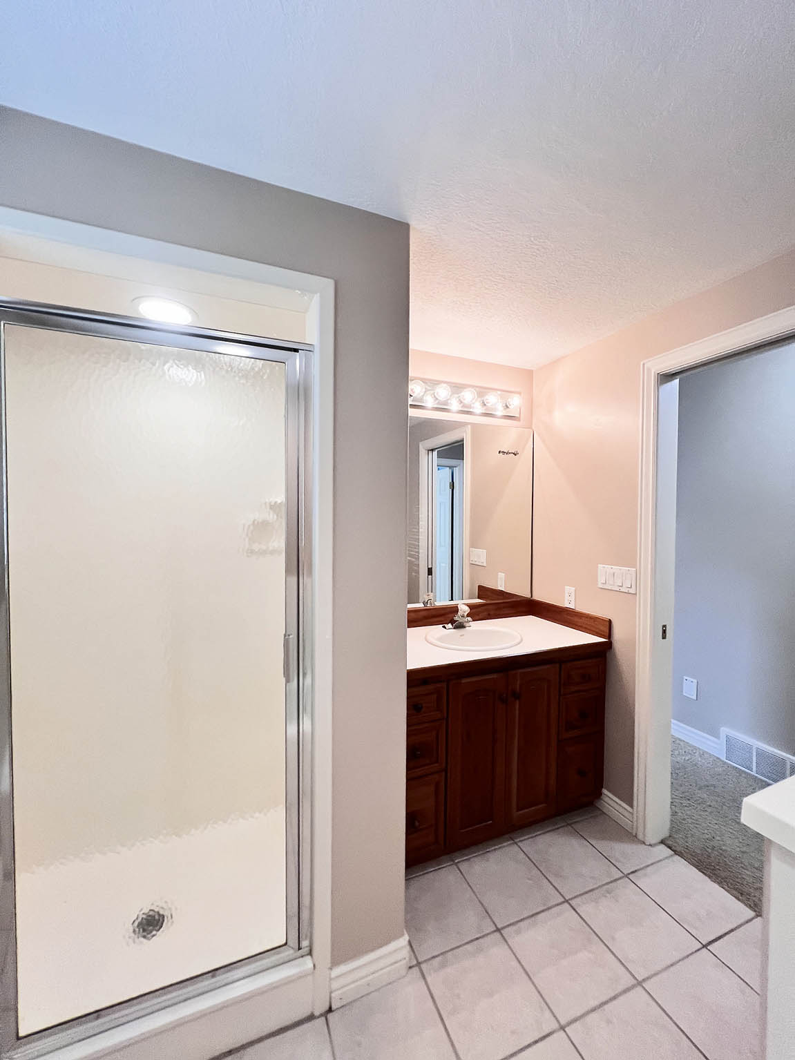 Bathroom featuring a frosted glass shower enclosure, a wood-finish vanity with a white countertop and integrated sink, and square tile flooring