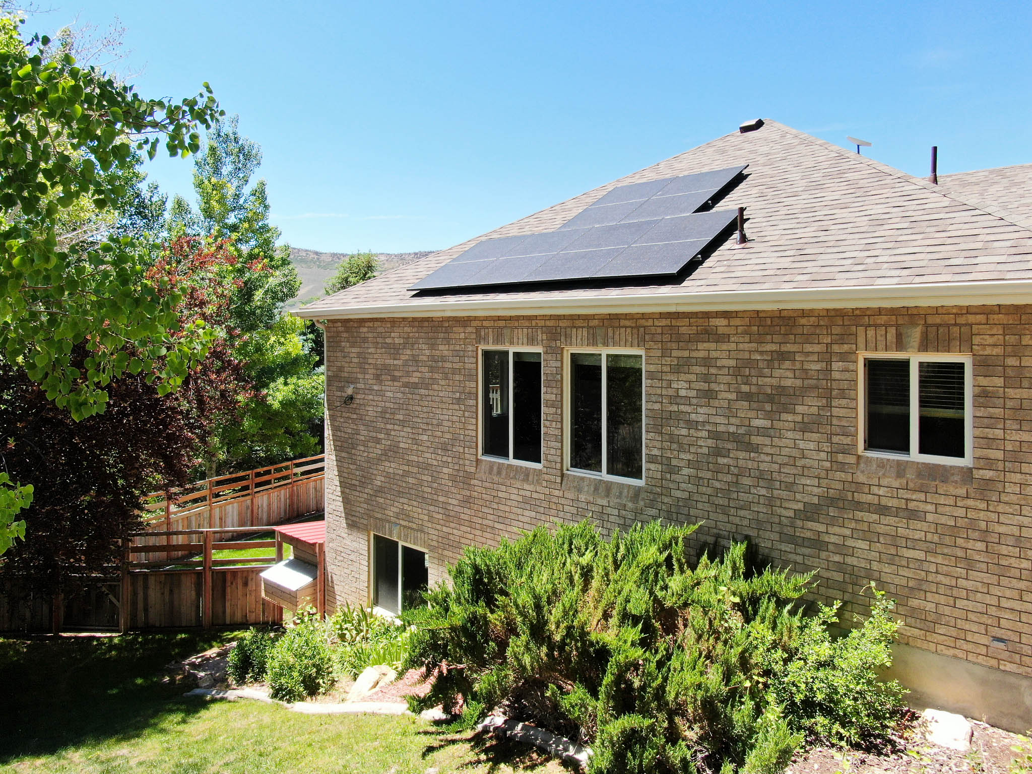 Brick exterior featuring a shingled roof with solar panels, multiple windows, and a lower-level sliding glass door