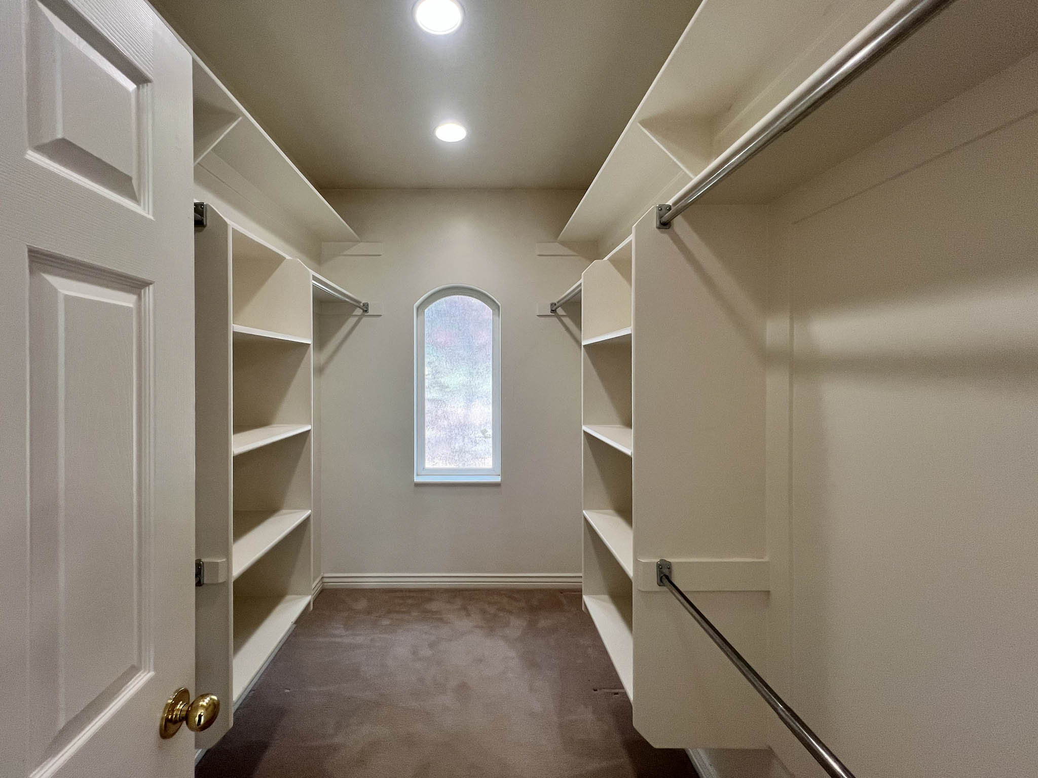 Walk-in closet with built-in shelving, hanging rods, recessed lighting, and an arched window