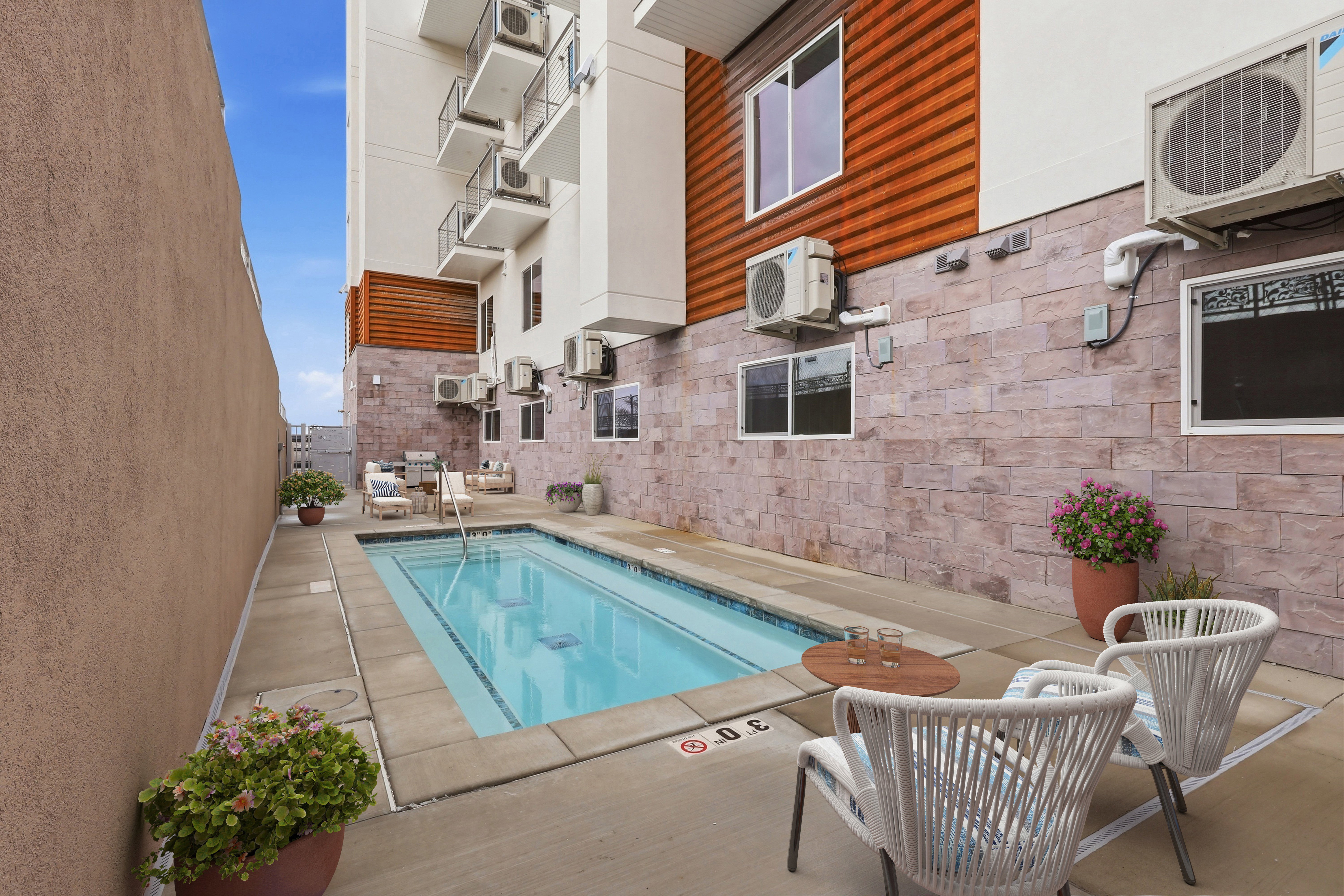 Outdoor swimming pool surrounded by concrete decking and textured wall finishes, featuring a multi-story building exterior with balconies