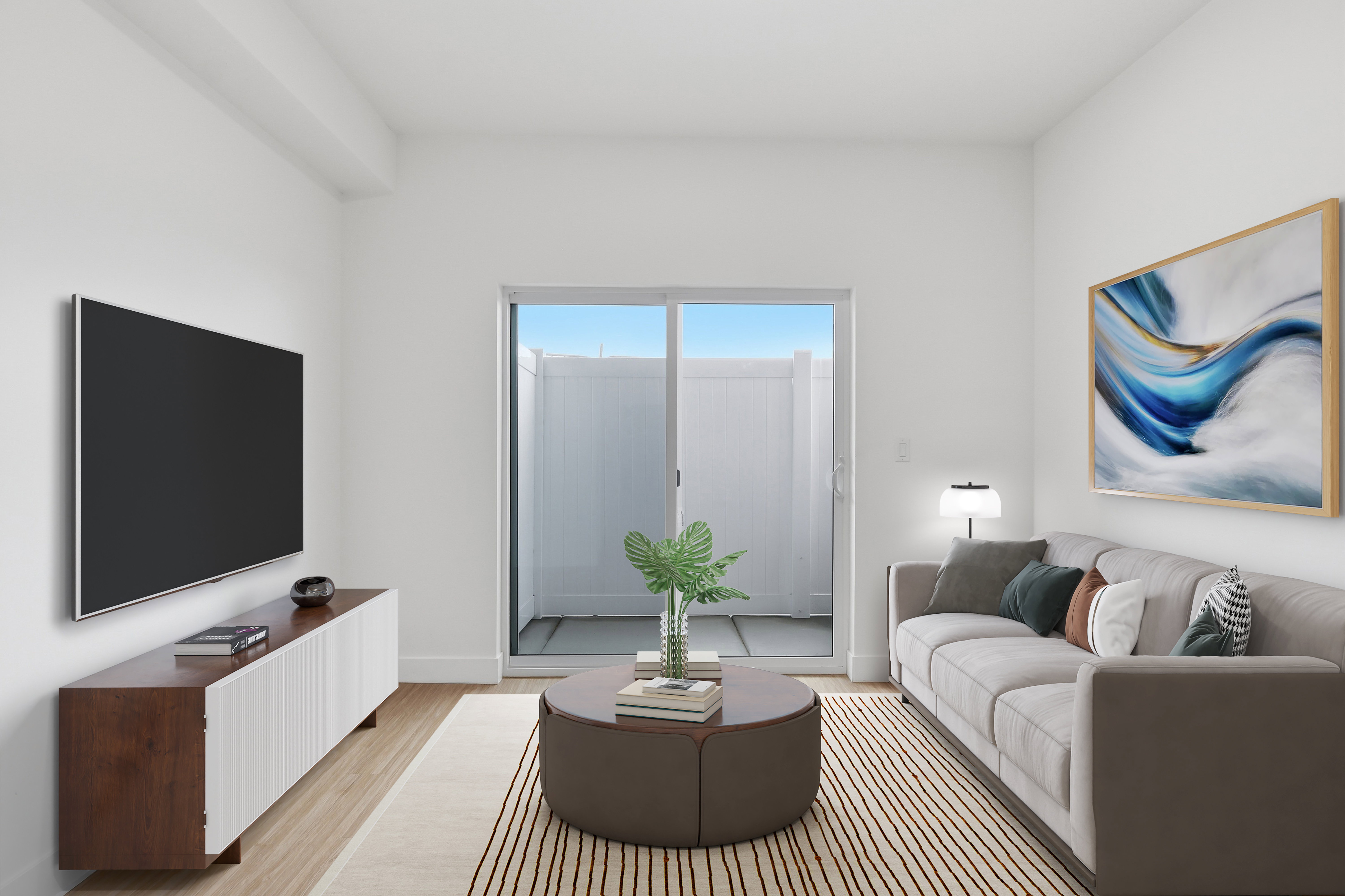 Living area featuring wood-finish flooring, a contemporary built-in media console, and a sliding glass door leading to an outdoor patio with privacy fencing