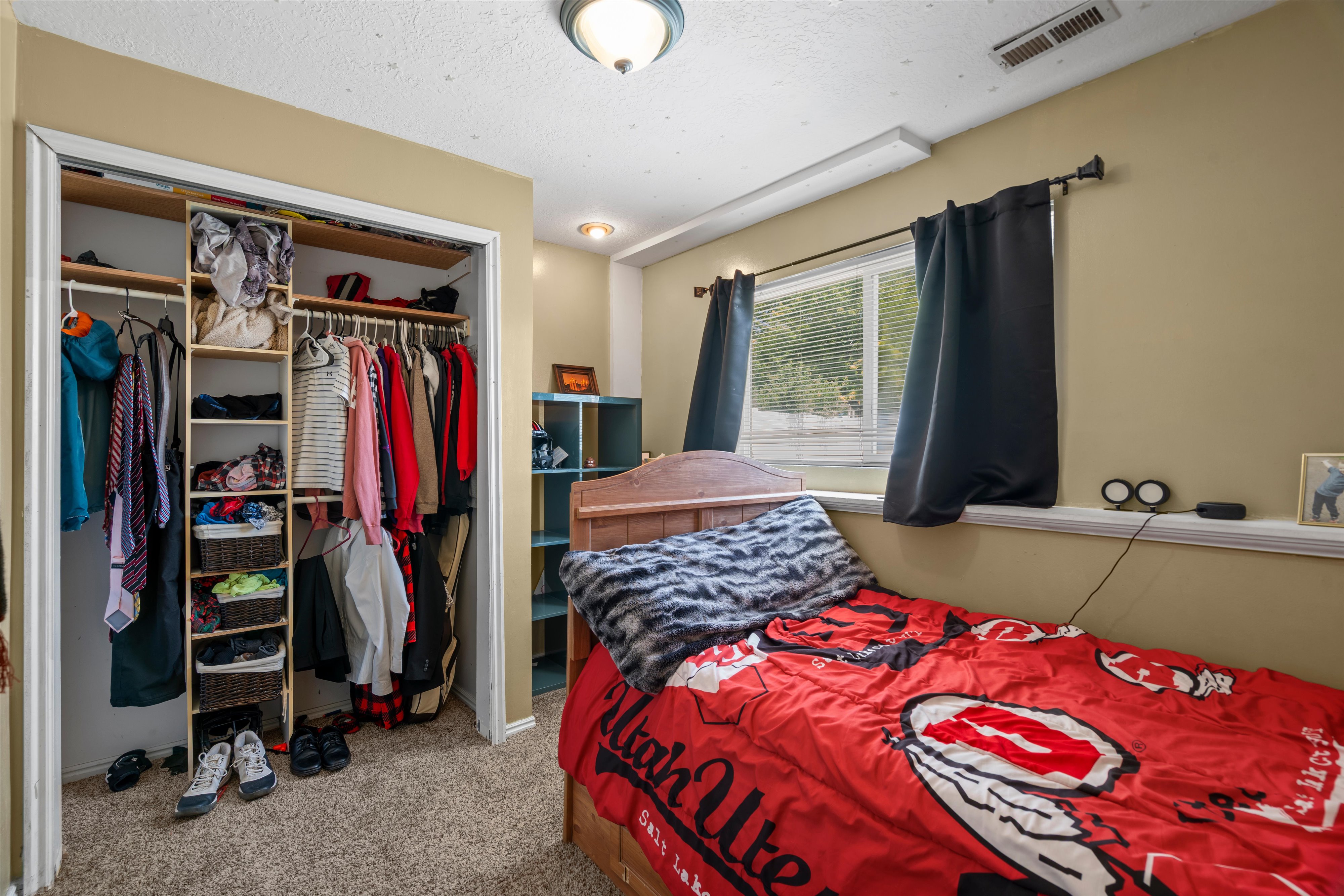 Bedroom featuring a built-in closet organization system, carpeted flooring, a window with horizontal blinds, and neutral wall tones