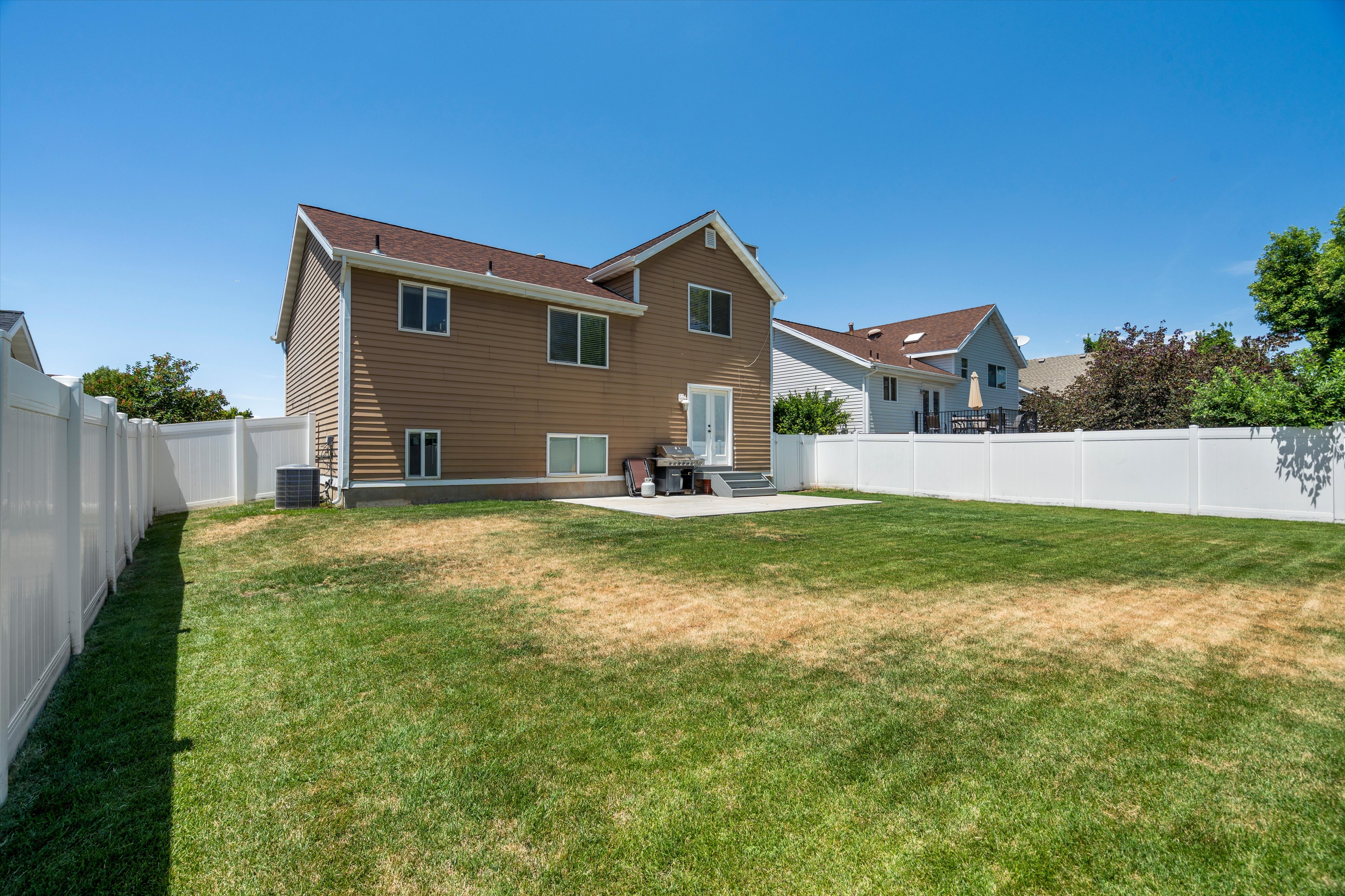 Expansive backyard featuring a manicured lawn, a concrete patio, and a white vinyl privacy fence