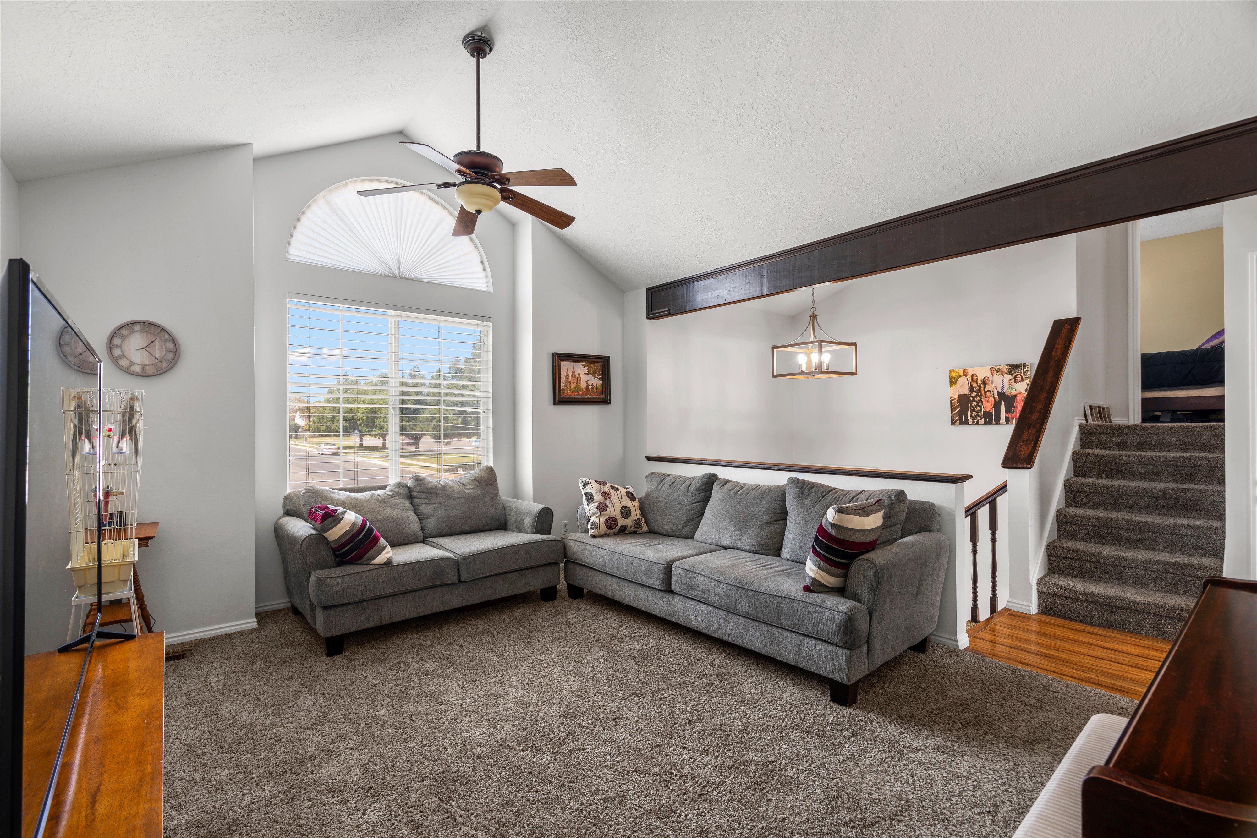 Vaulted ceiling living area featuring a large arched window with blinds, a ceiling fan, and carpeted flooring