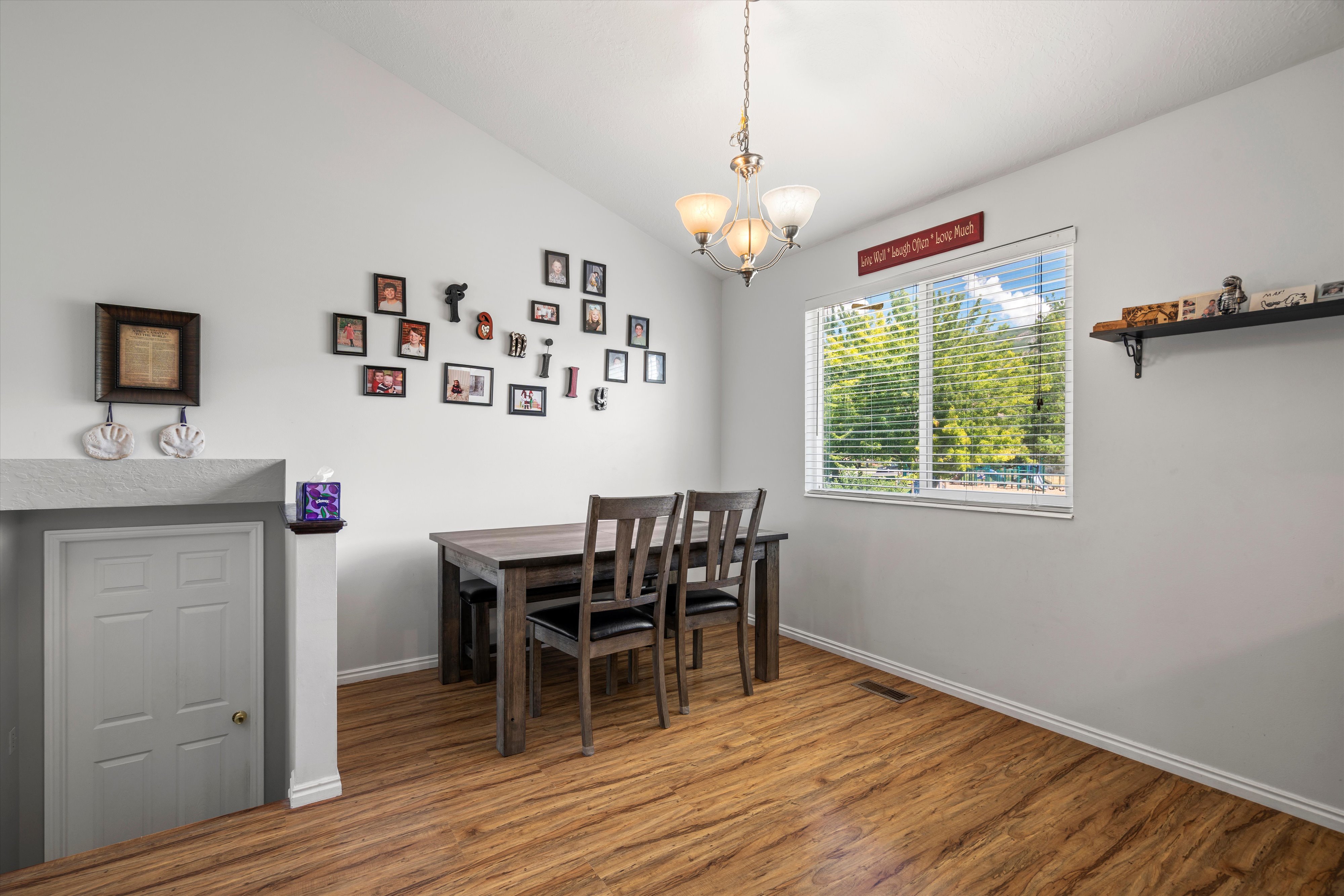 Vaulted ceiling room featuring wood-finish flooring and a multi-pane window with horizontal blinds