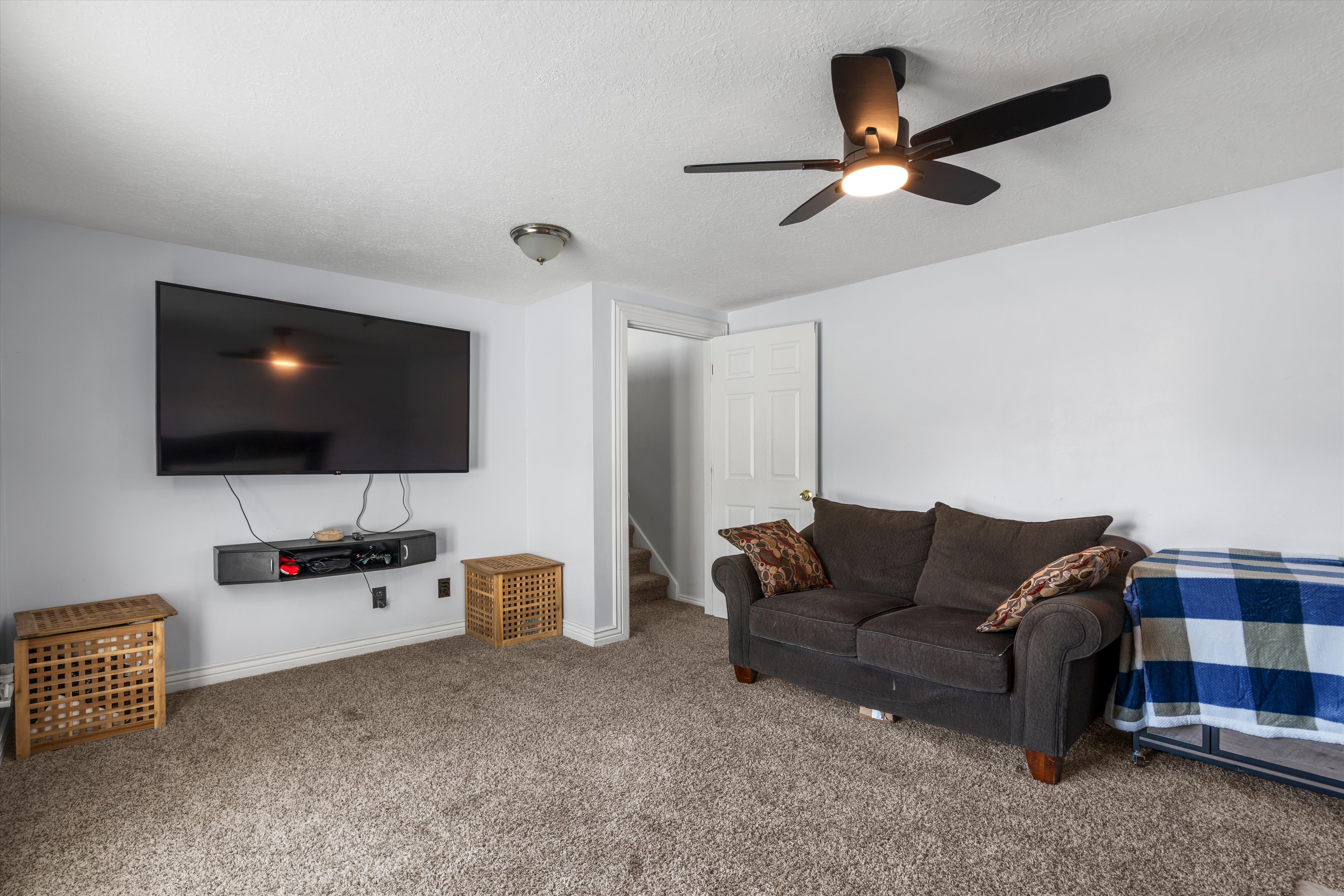 Carpeted room featuring a ceiling fan with integrated lighting, a wall-mounted media console, and a flush-mount ceiling light