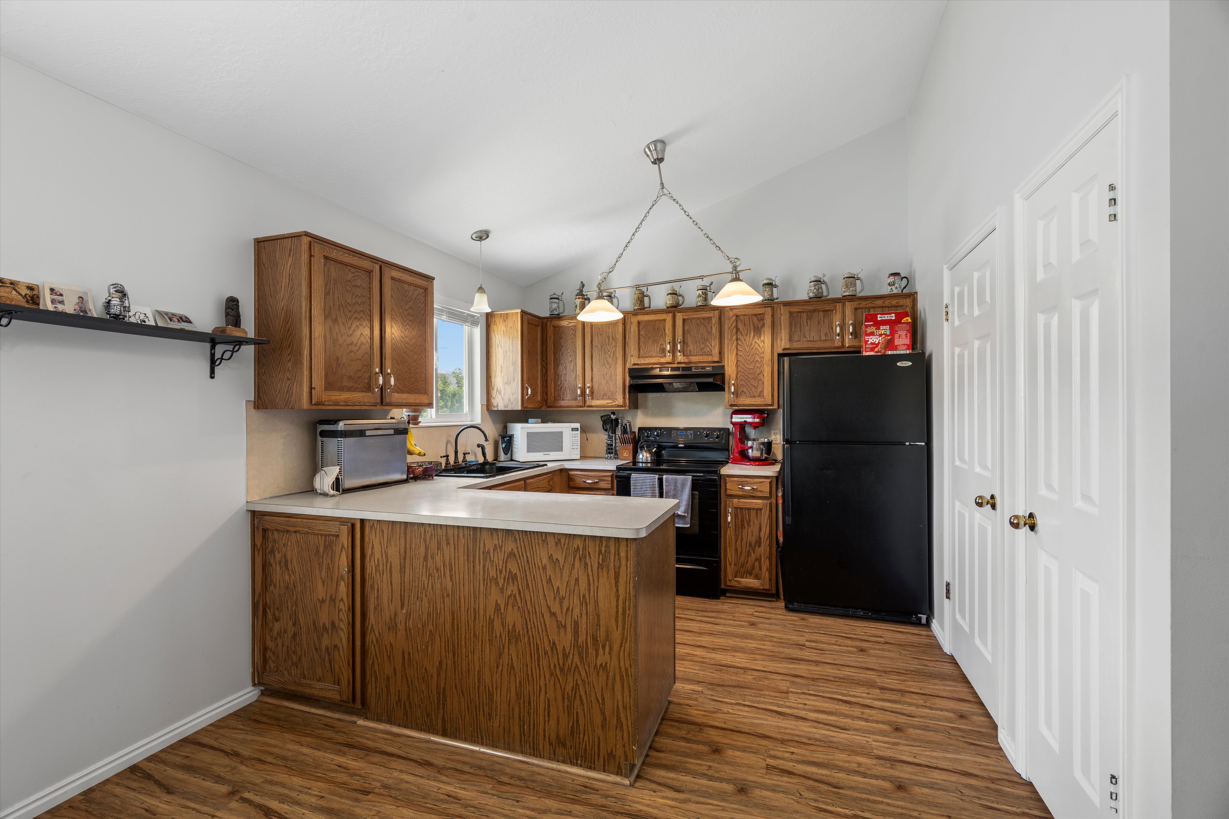 Kitchen featuring wood-finish flooring, wood cabinetry, light-toned countertops, a black appliance suite, and a vaulted ceiling with pendant lighting