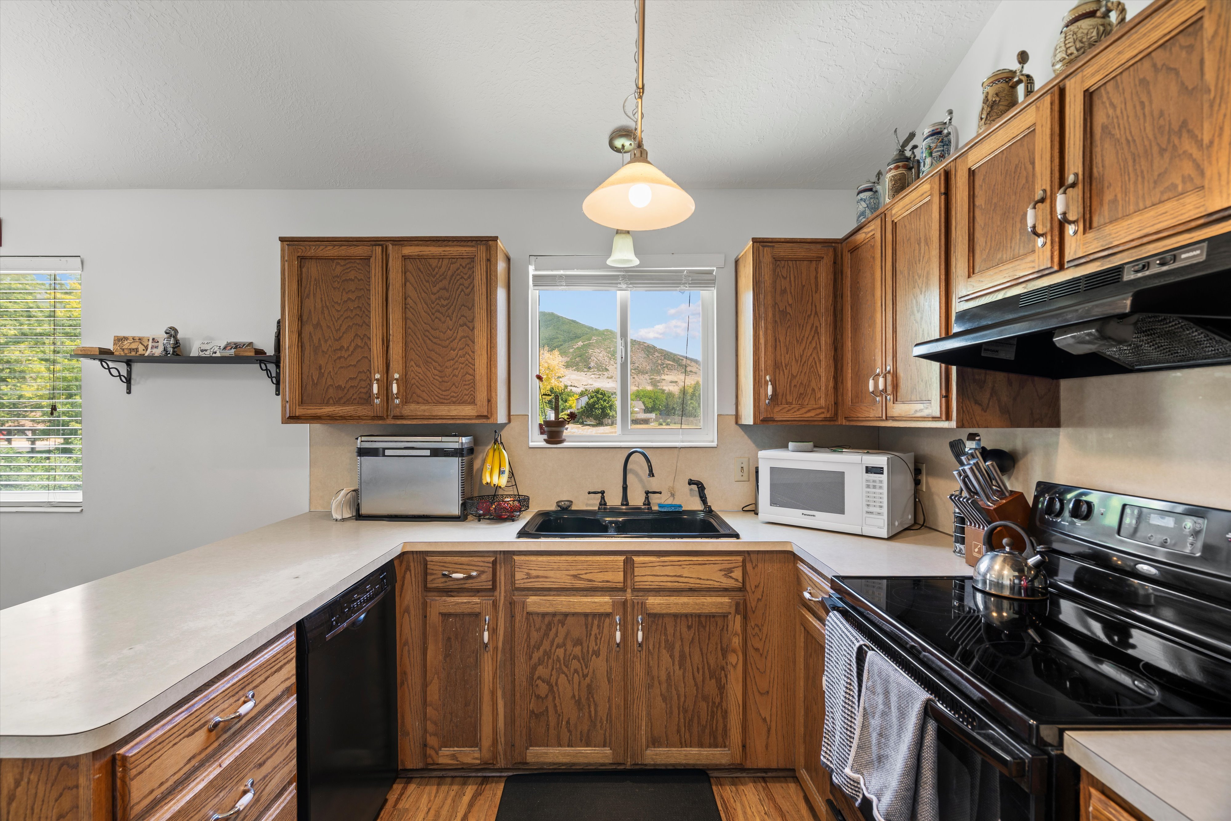 Kitchen featuring wood cabinetry, light-toned countertops, a black electric range, and a black sink with a window overlooking mountainous scenery