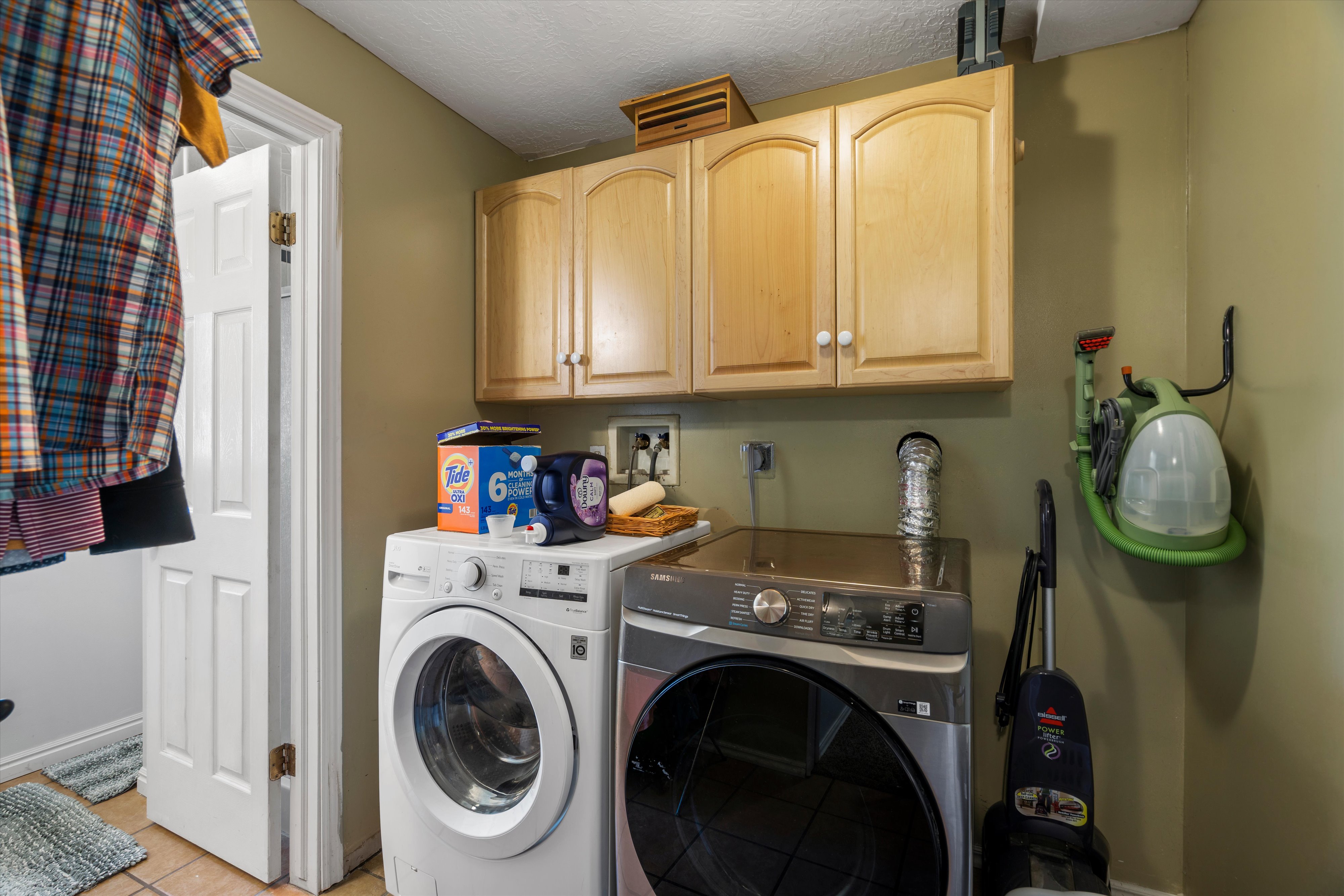 Dedicated laundry space featuring upper cabinetry with wood-finish doors and brushed nickel hardware