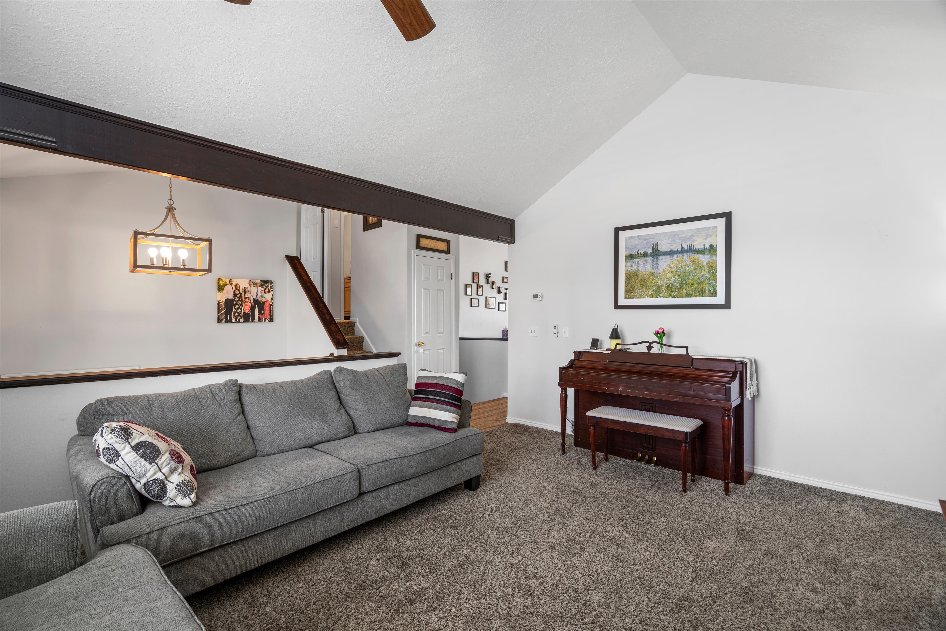 Spacious living area featuring a vaulted ceiling, exposed beam, carpeted flooring, and a ceiling fan