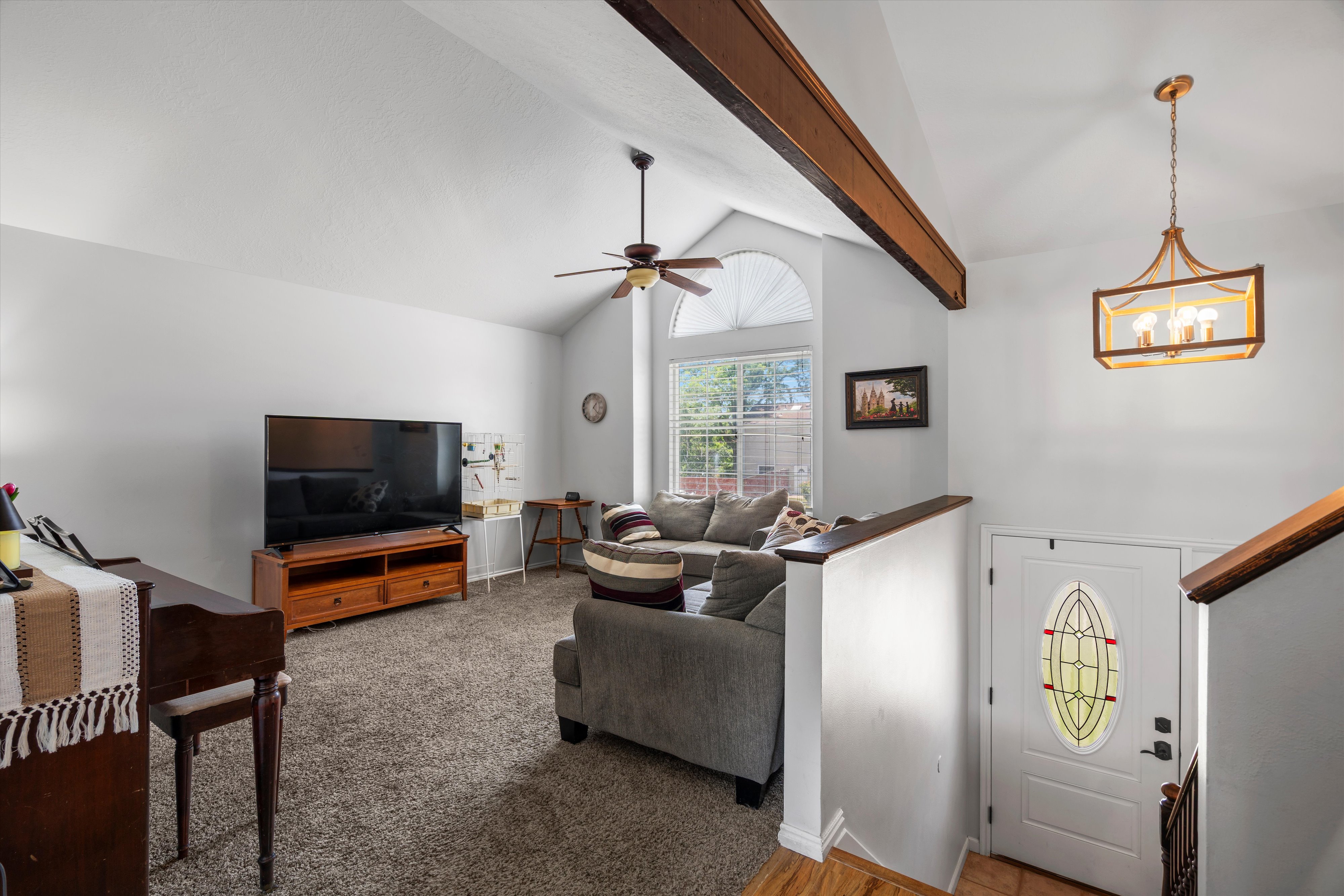 Spacious living area featuring vaulted ceilings with exposed wood beams, a prominent arched window, and plush carpeting