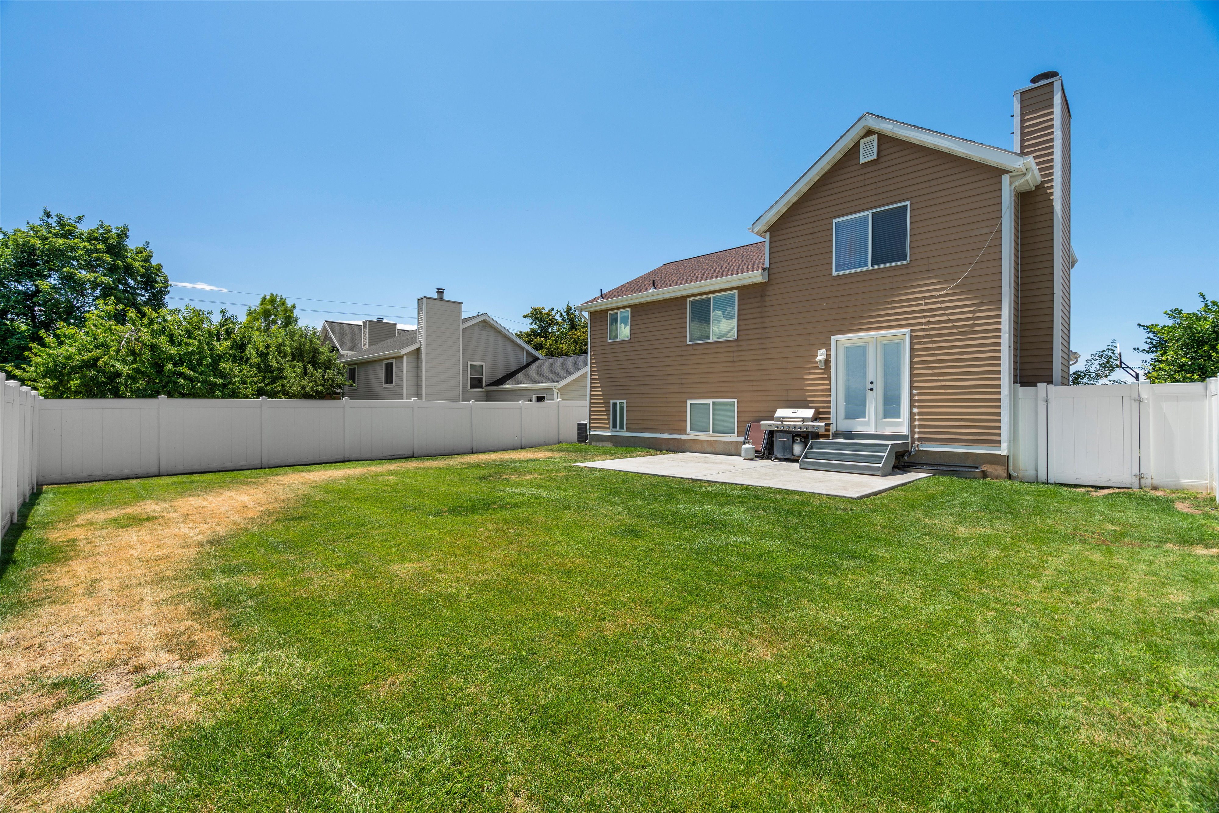 Expansive backyard featuring a privacy fence, concrete patio, and mature trees