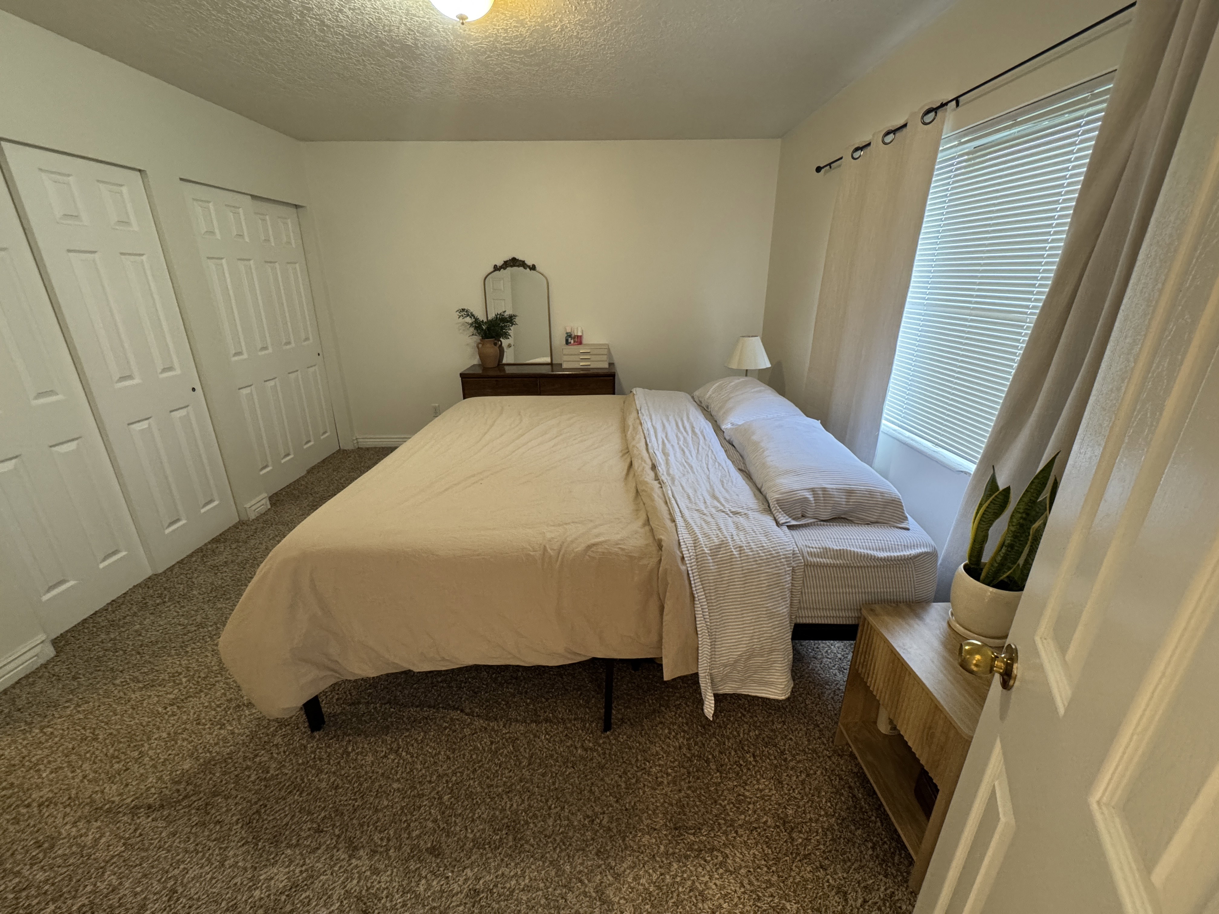 Carpeted room featuring an overhead light fixture, window with blinds, and white bi-fold closet doors