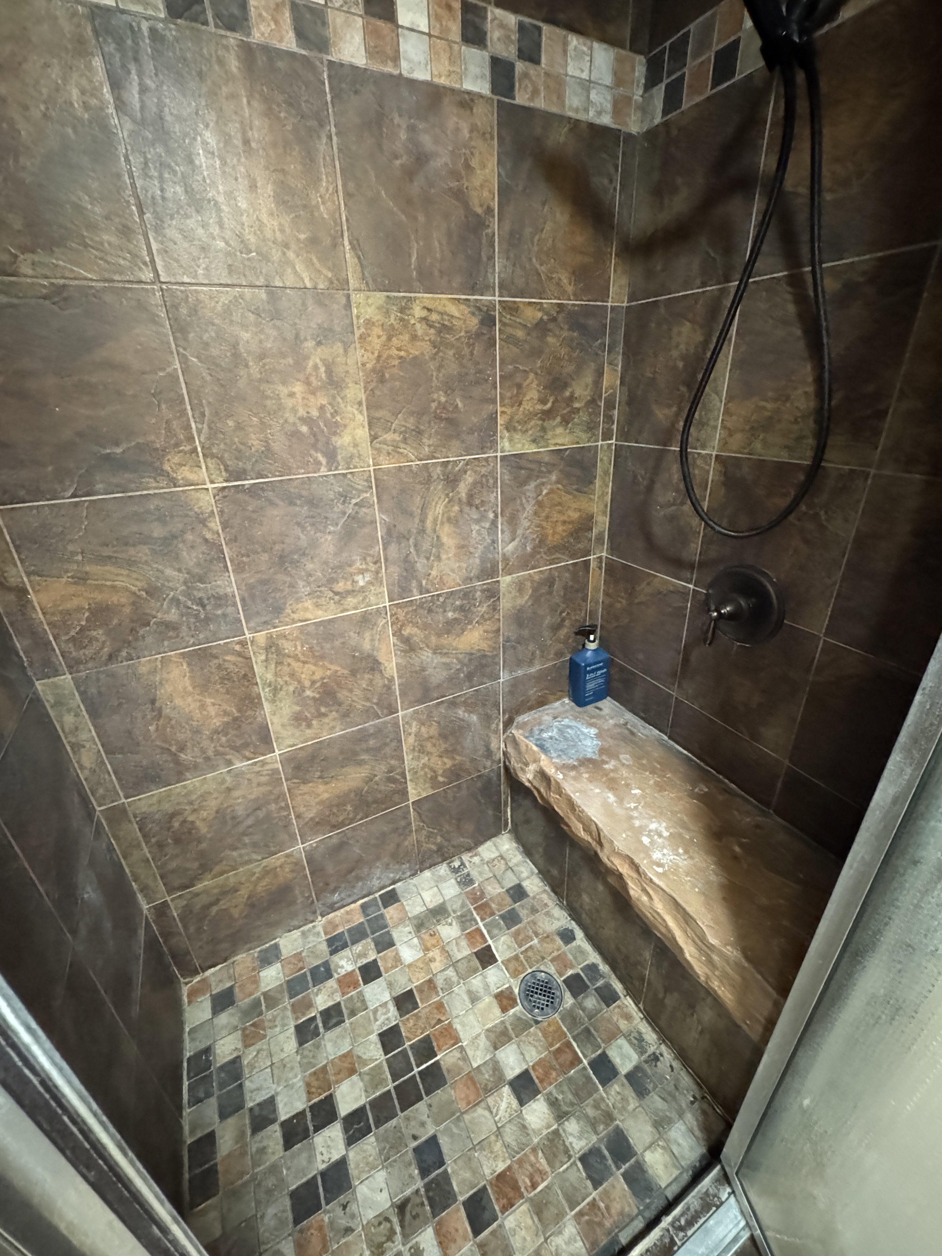 Tiled shower with a built-in stone bench, featuring a multi-toned mosaic floor and a decorative tile border