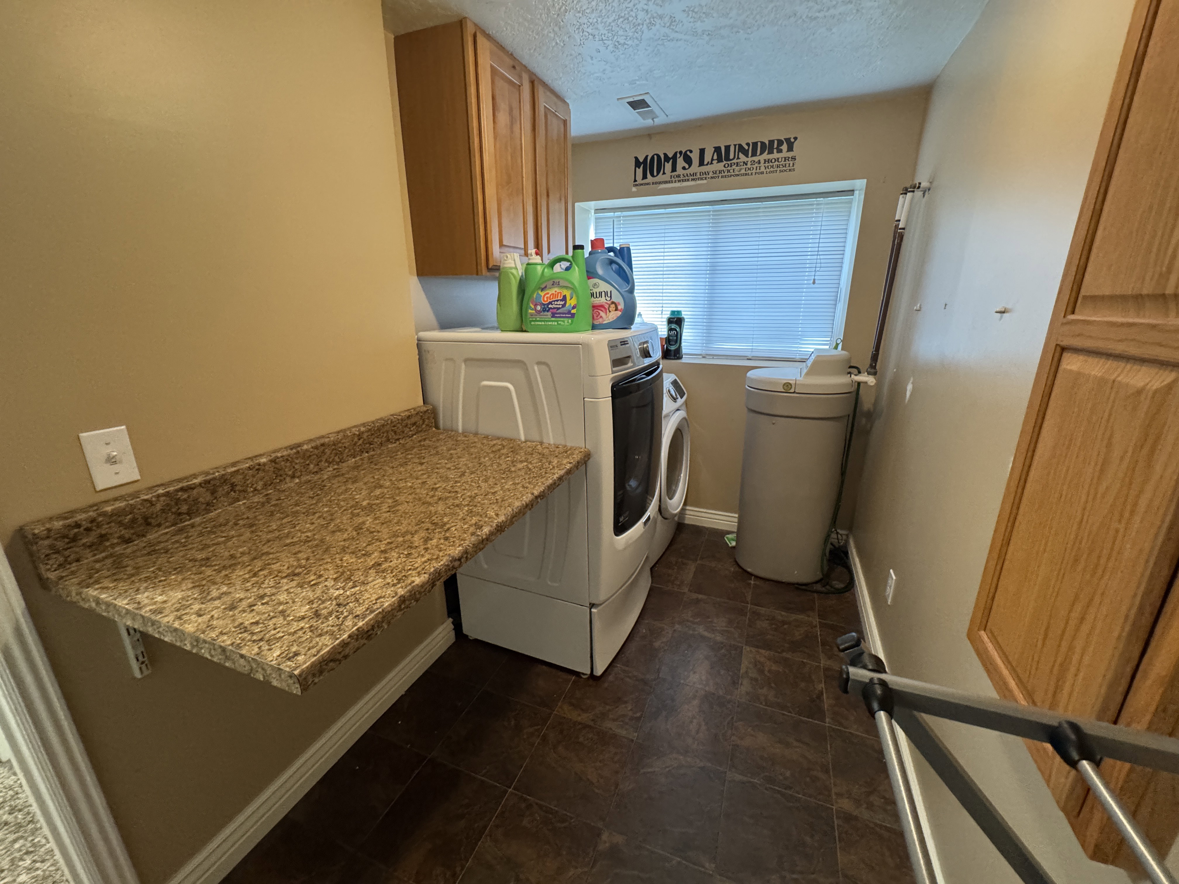 Dedicated laundry room featuring wood-finish cabinetry, a window with blinds, and vinyl flooring