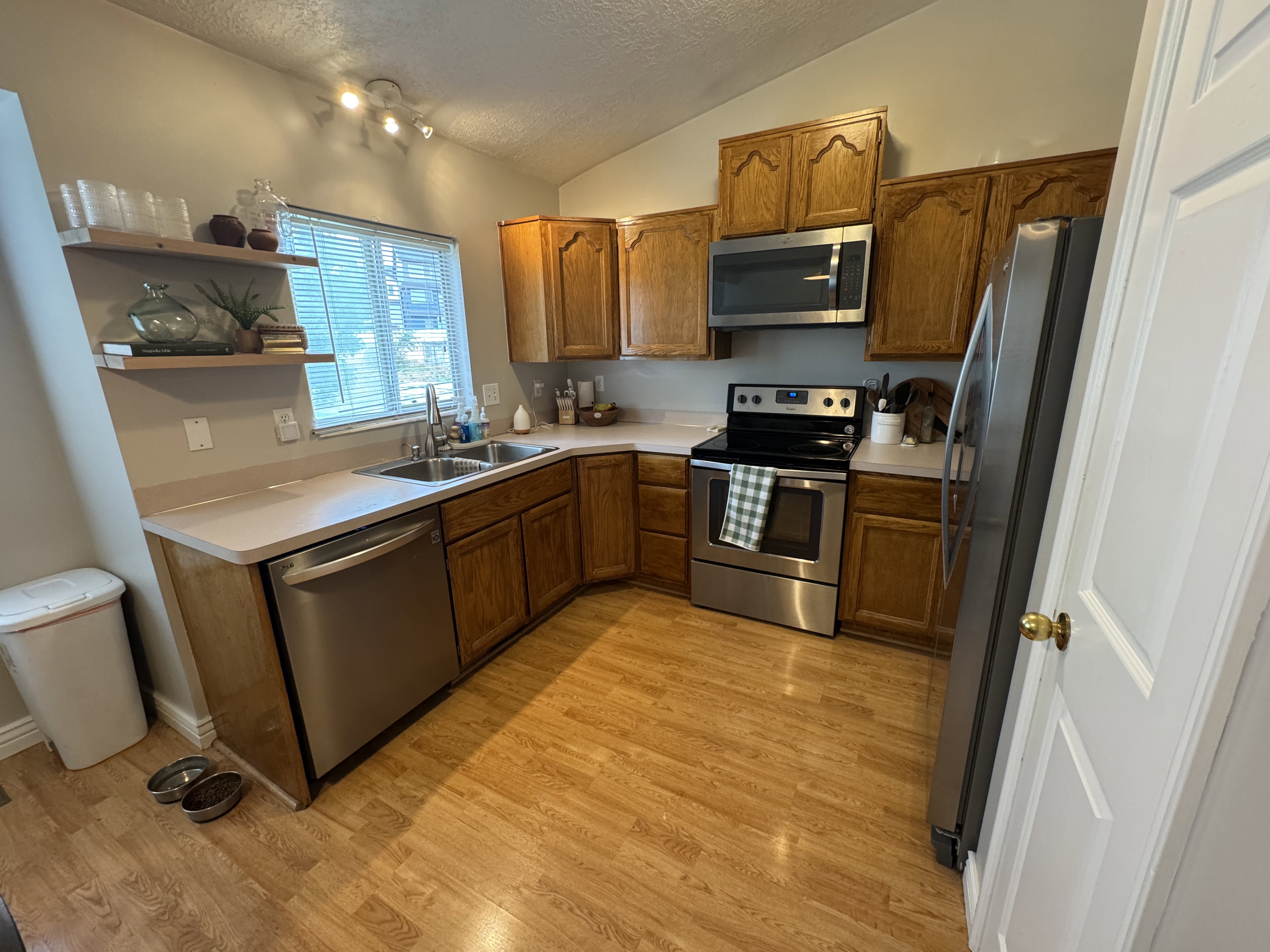Kitchen featuring wood-finish flooring, oak cabinetry, light-toned countertops, and stainless steel appliances including a range, dishwasher, microwave, and refrigerator