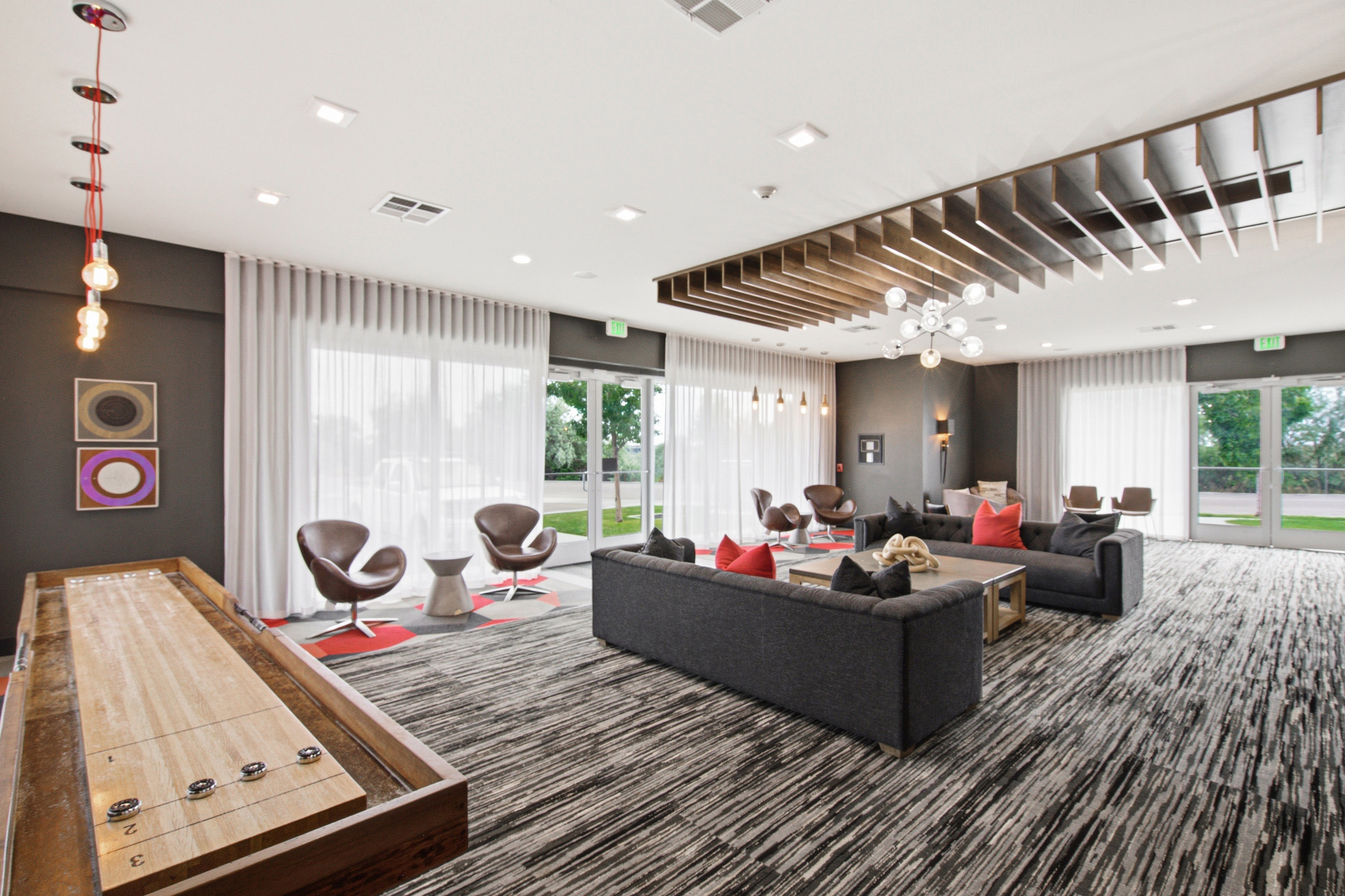 Spacious common area featuring an expansive patterned carpet, full-height windows with sheer drapery, and multiple modern light fixtures