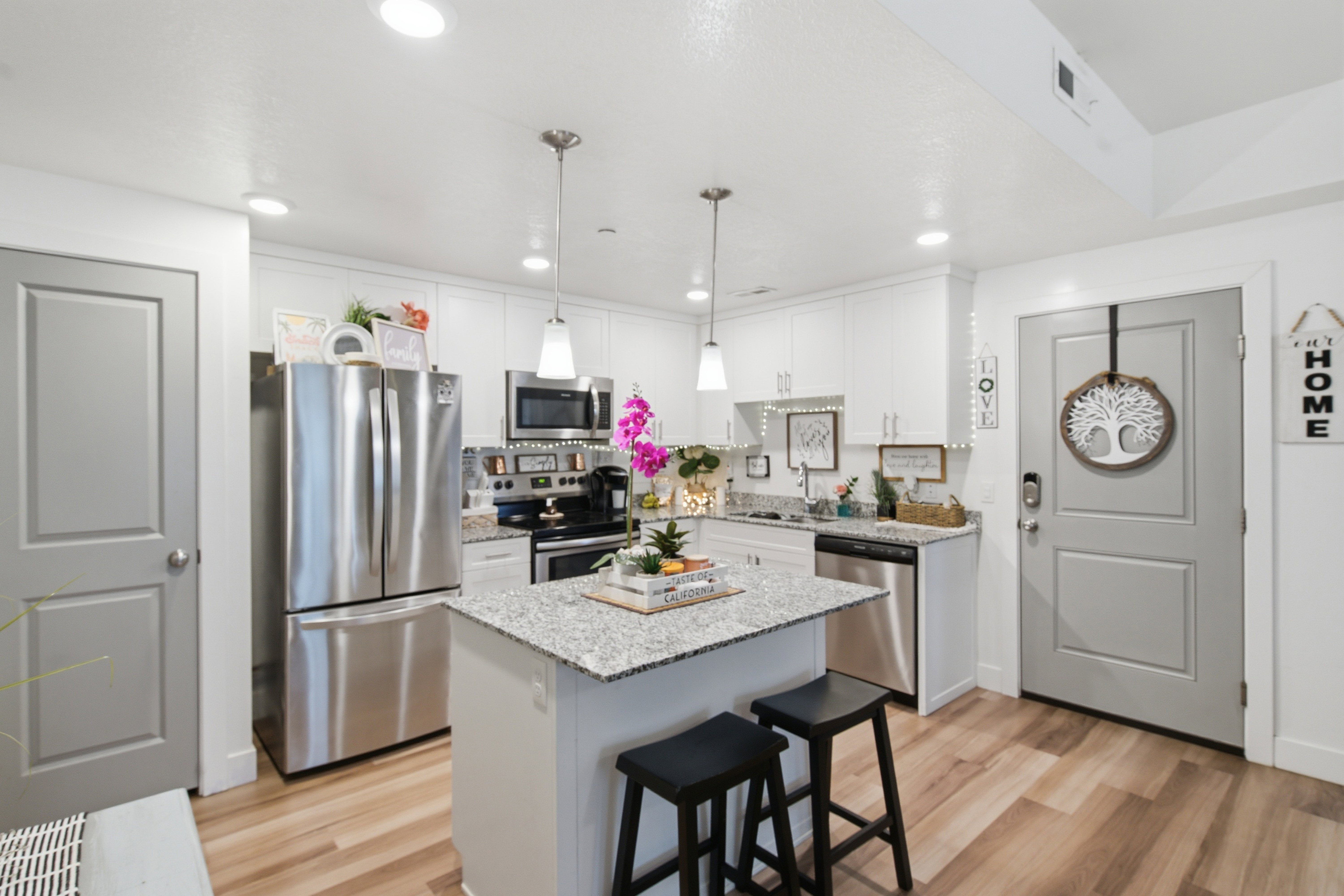 Modern kitchen featuring white cabinetry, stainless steel appliances, a granite countertop island with seating, pendant lighting, and wood-finish flooring