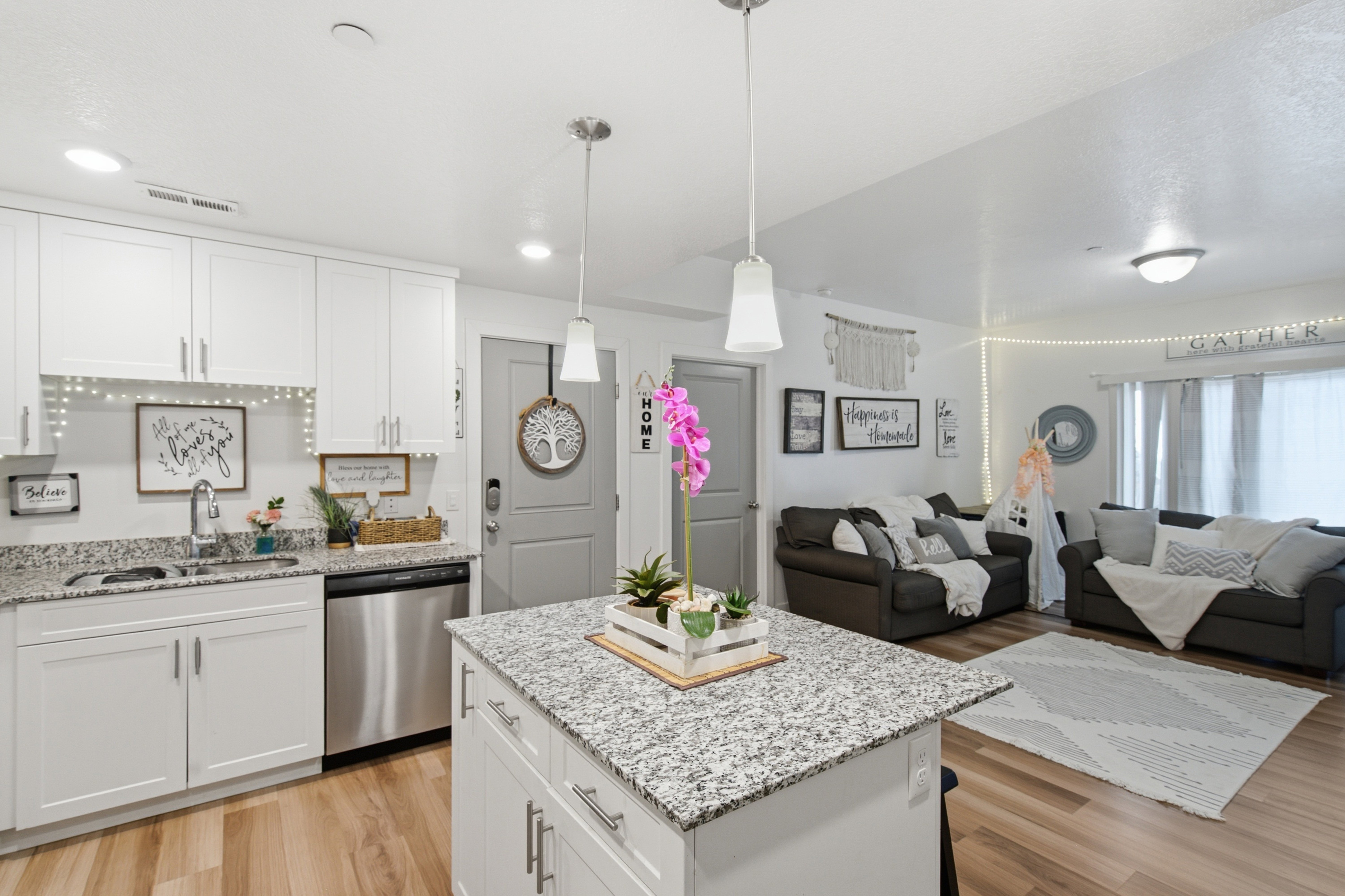 Open-concept living area featuring a kitchen island with stone-finish countertops, white cabinetry, stainless steel dishwasher, wood-finish flooring, and recessed lighting