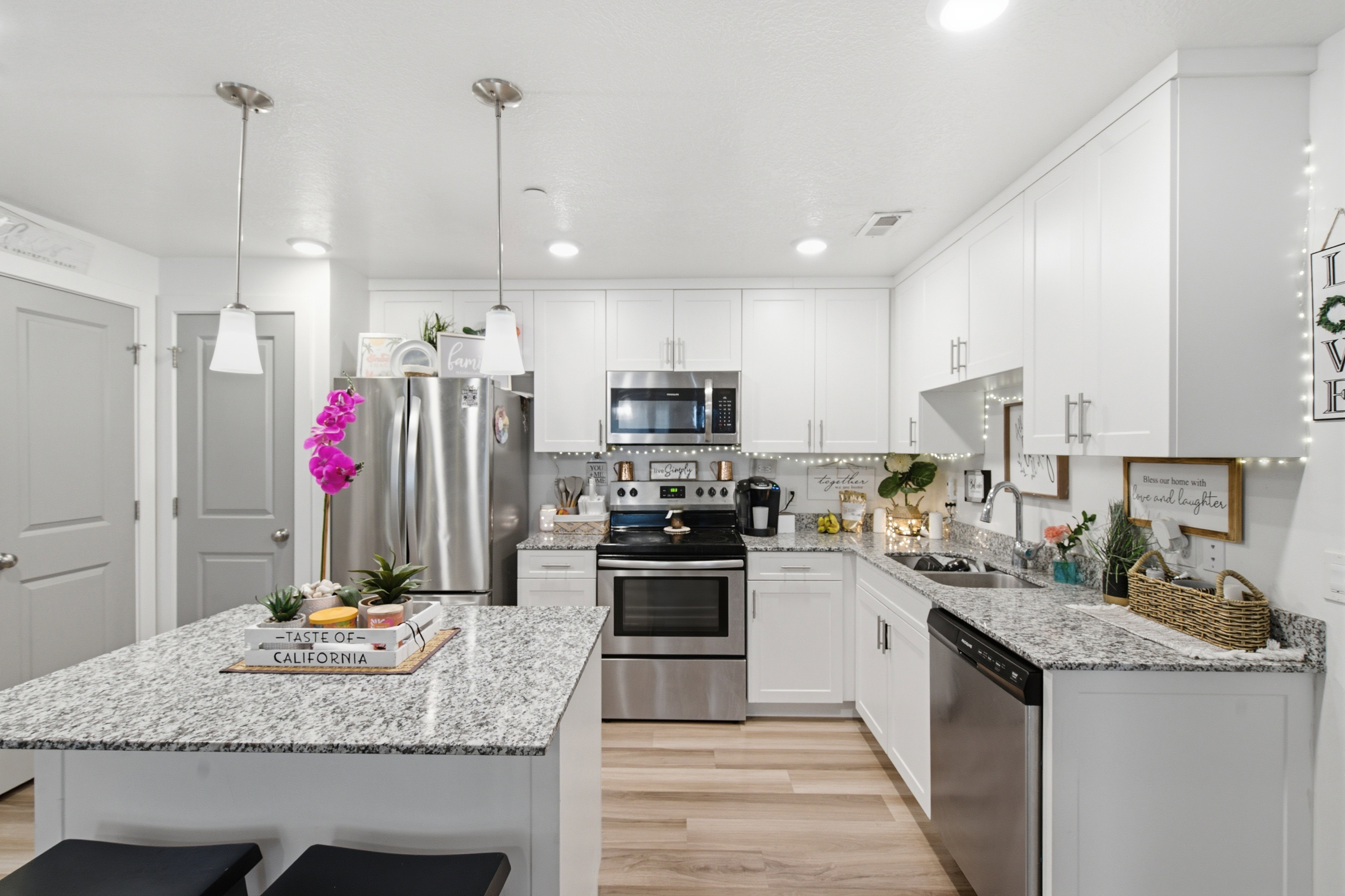 Modern kitchen featuring a central island with granite countertop, white cabinetry, stainless steel appliances, and wood-finish flooring