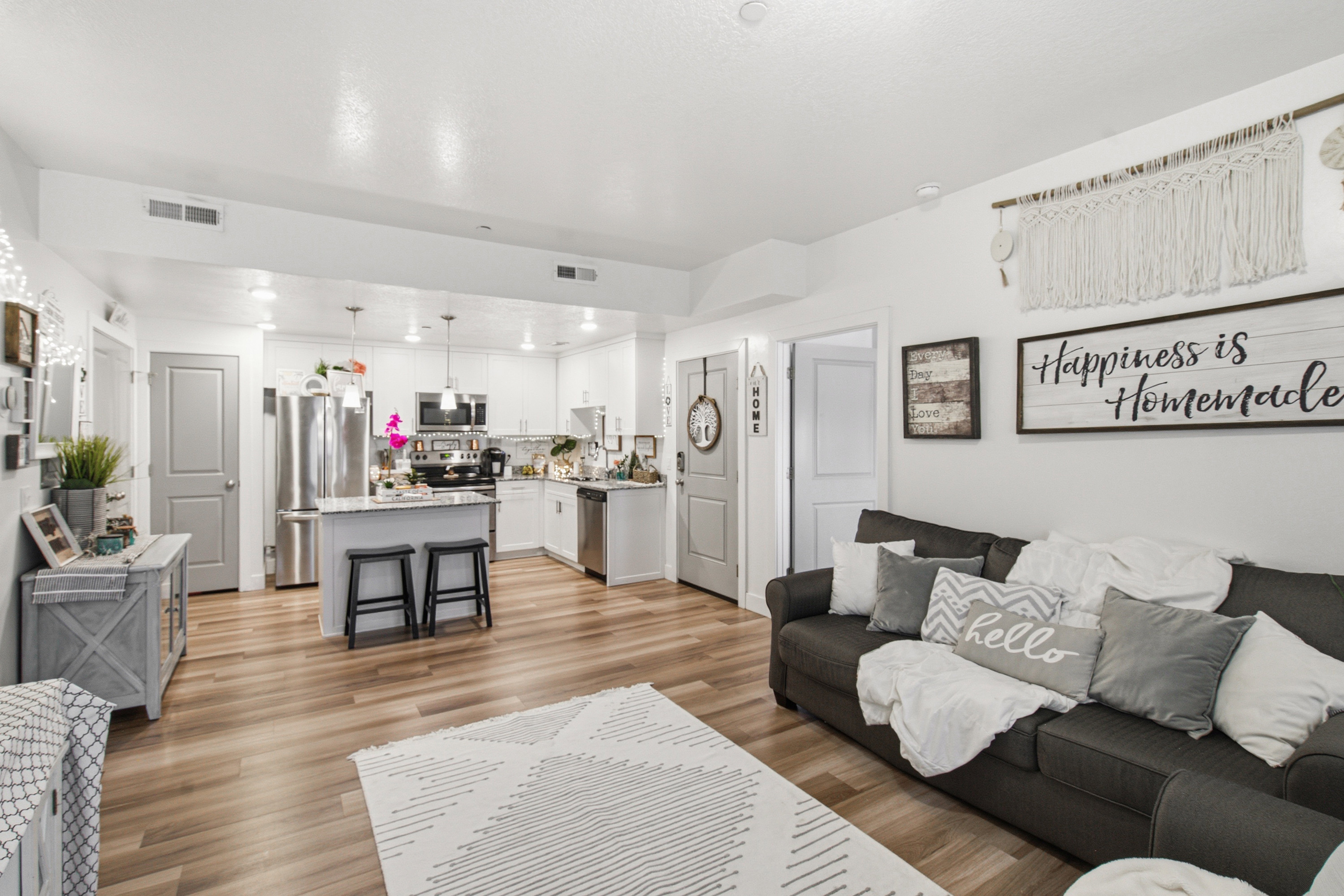 Open-concept living space featuring wood-finish flooring, a contemporary kitchen with white cabinetry, stainless steel appliances, a kitchen island with seating, and recessed lighting