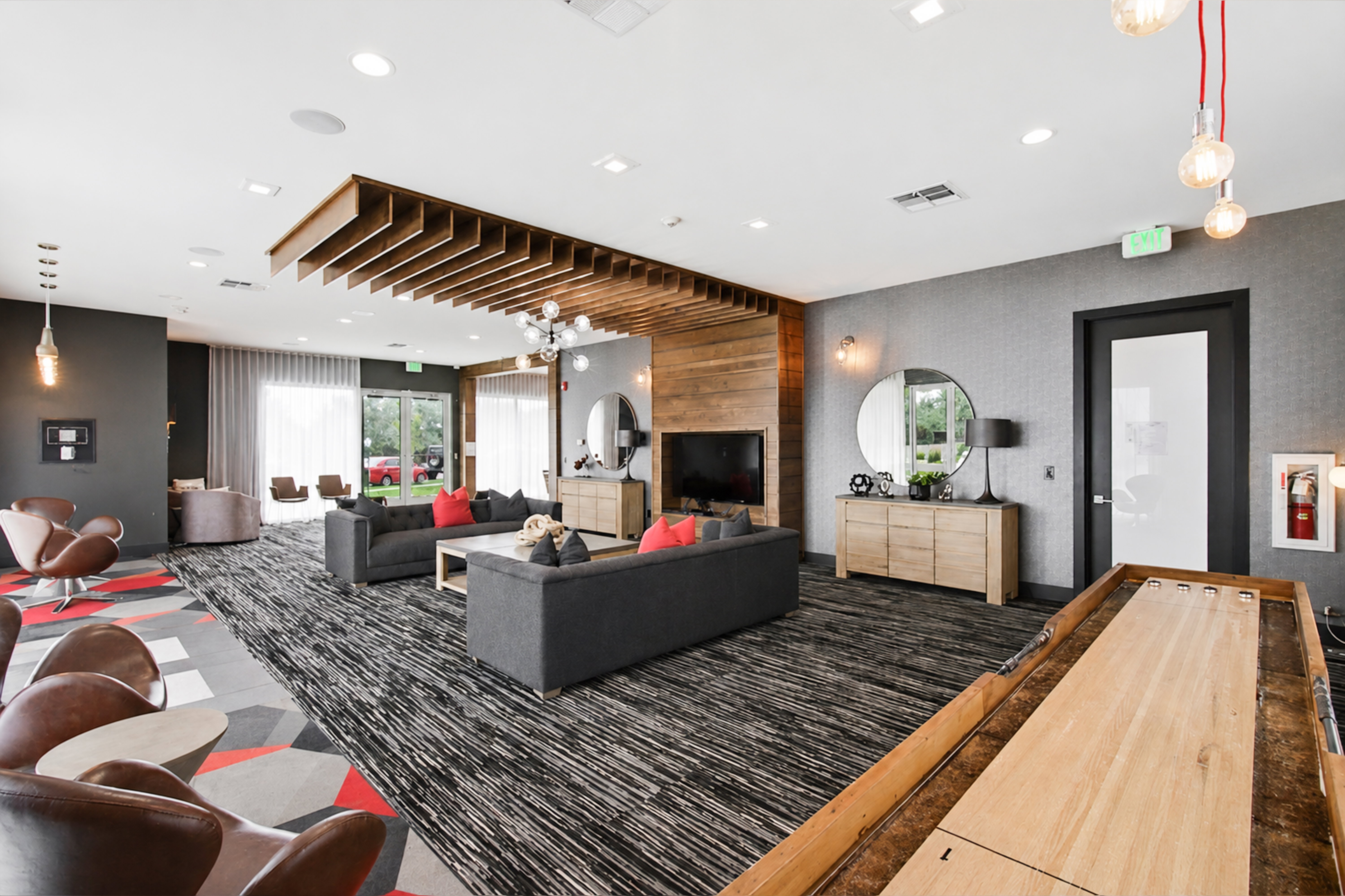 Spacious common area featuring patterned carpet flooring, a decorative wood slat ceiling element, and large windows