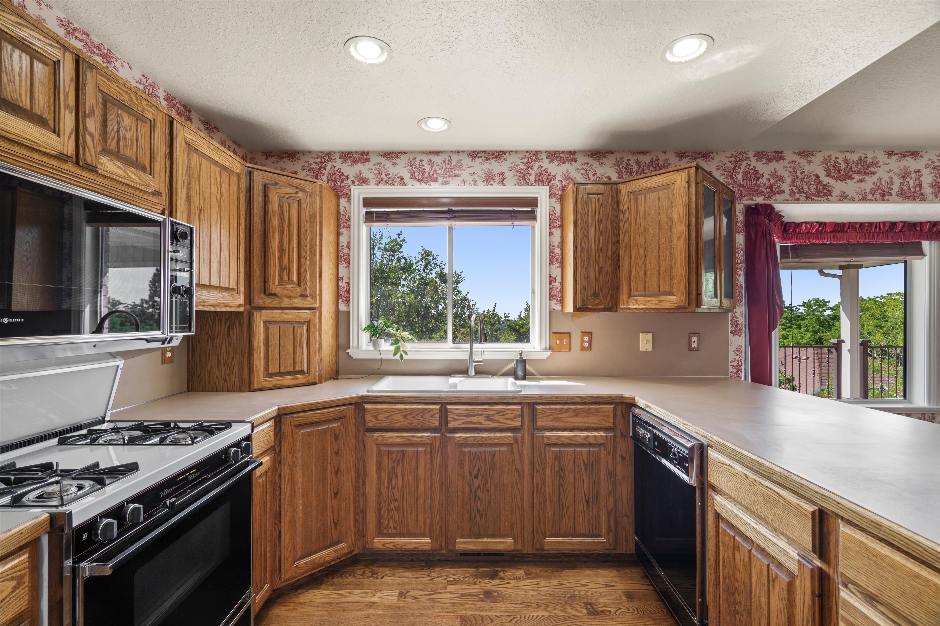 Kitchen featuring wood-finish cabinetry, a white gas range with an overhead microwave, a window over the sink, and a dishwasher