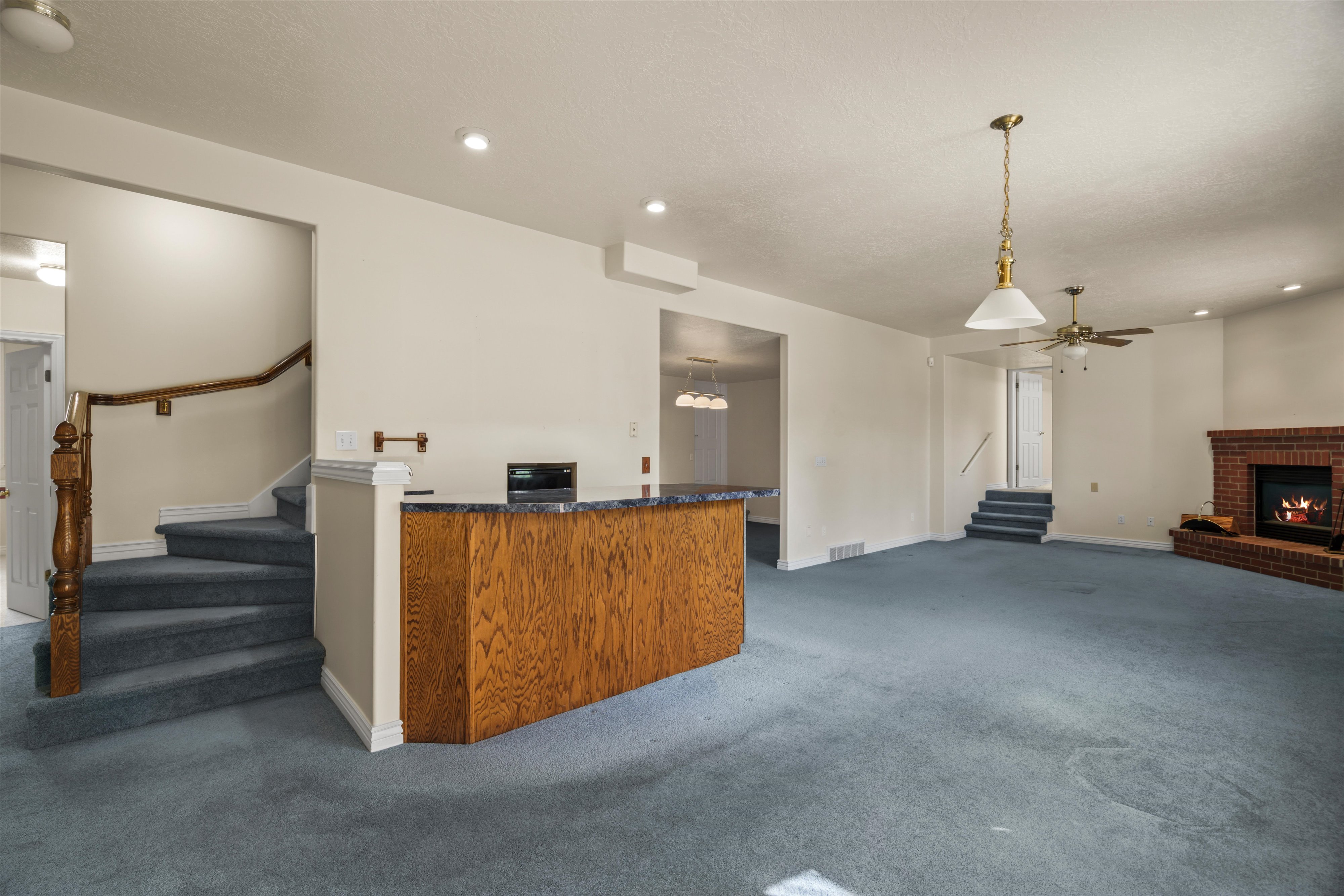 Spacious open-concept living area featuring an integrated wood-paneled wet bar with a dark countertop, a brick fireplace, and a ceiling fan