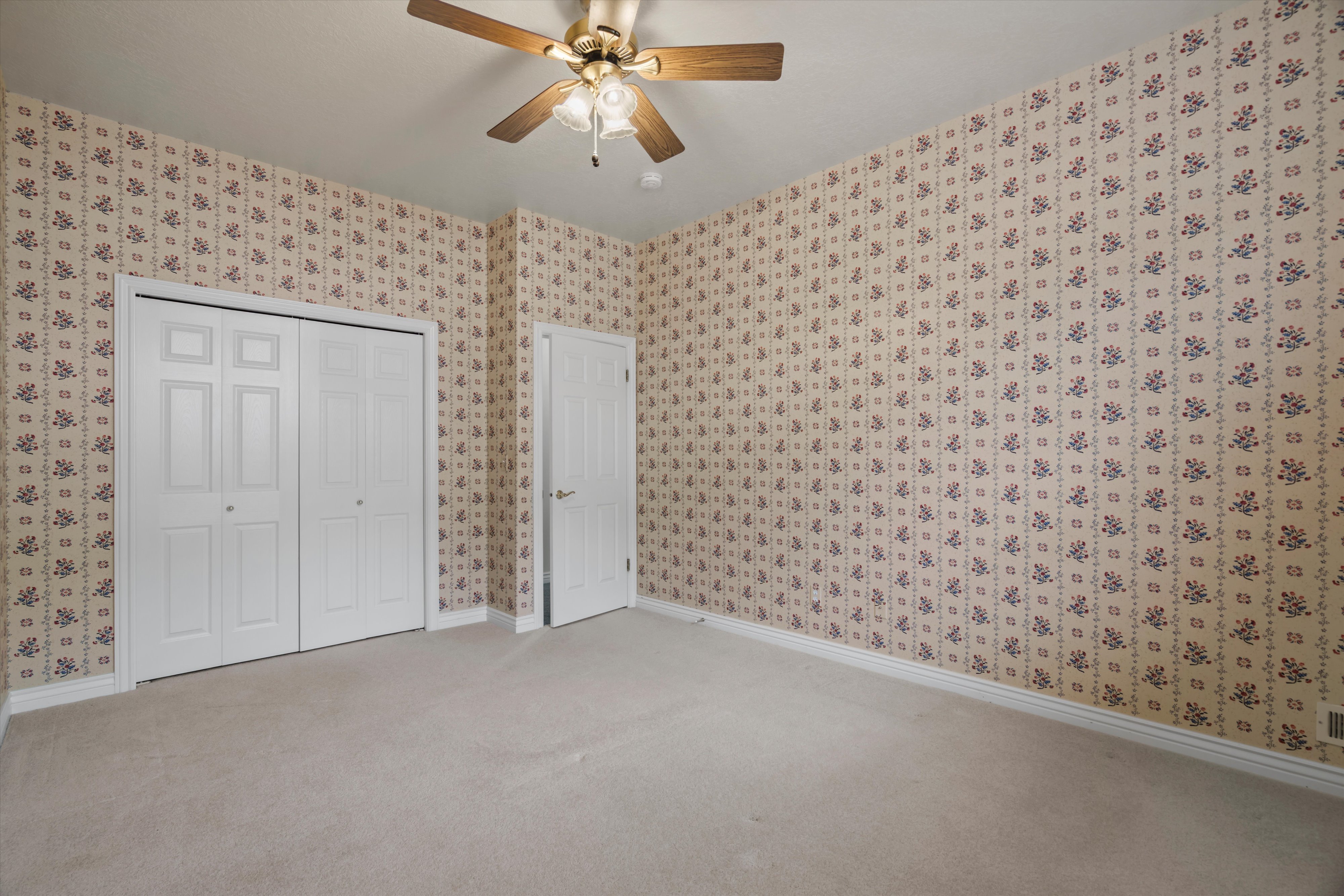 Room with patterned wallpaper, light-colored carpeting, and a ceiling fan with integrated lighting