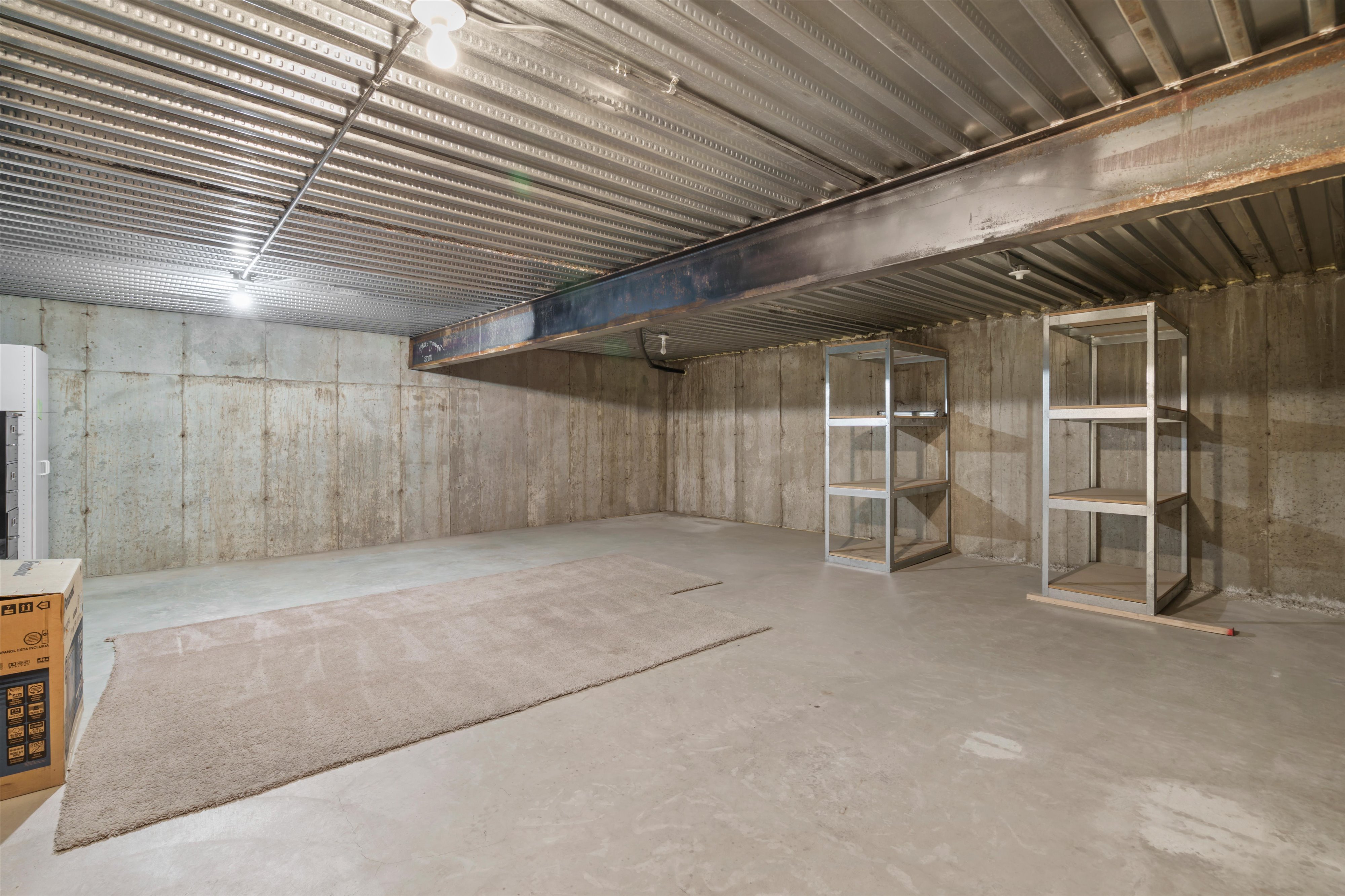 Expansive unfinished lower level featuring exposed concrete walls and ceiling with a large support beam