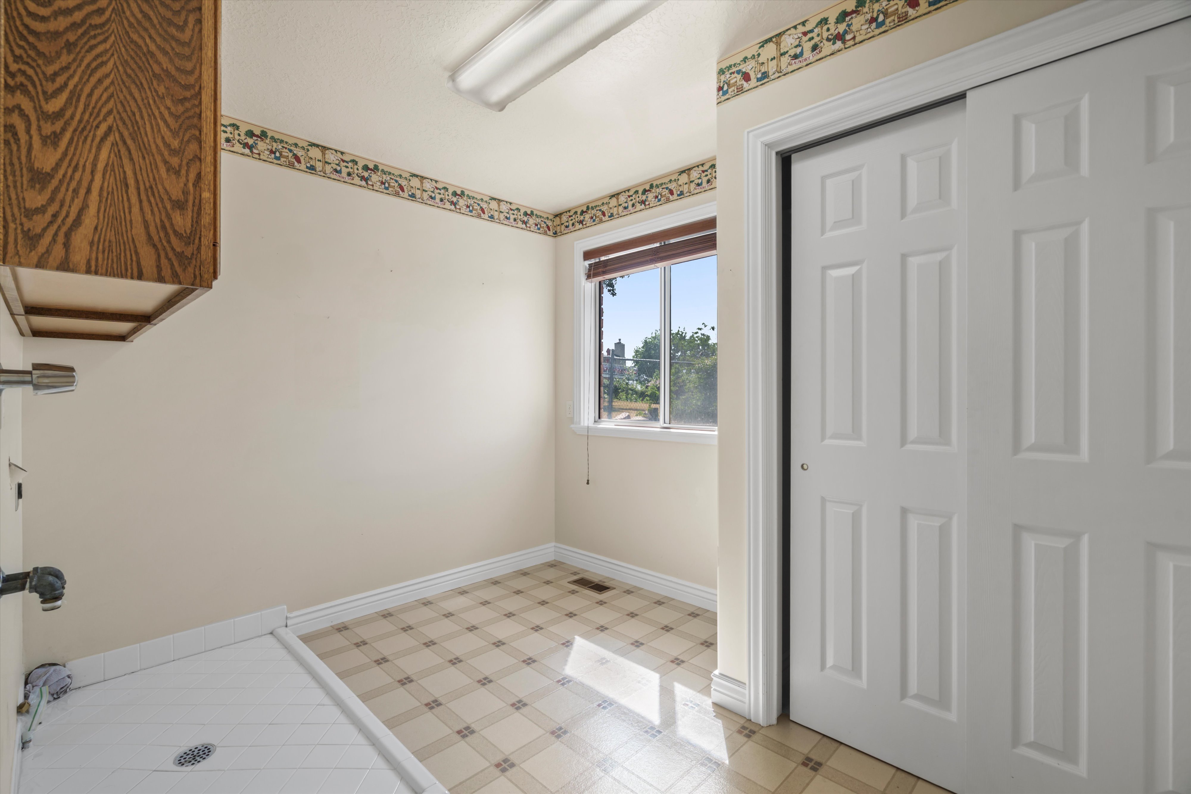 Utility room featuring a window with natural light, tiled flooring, wood-finish cabinetry, and a built-in utility sink