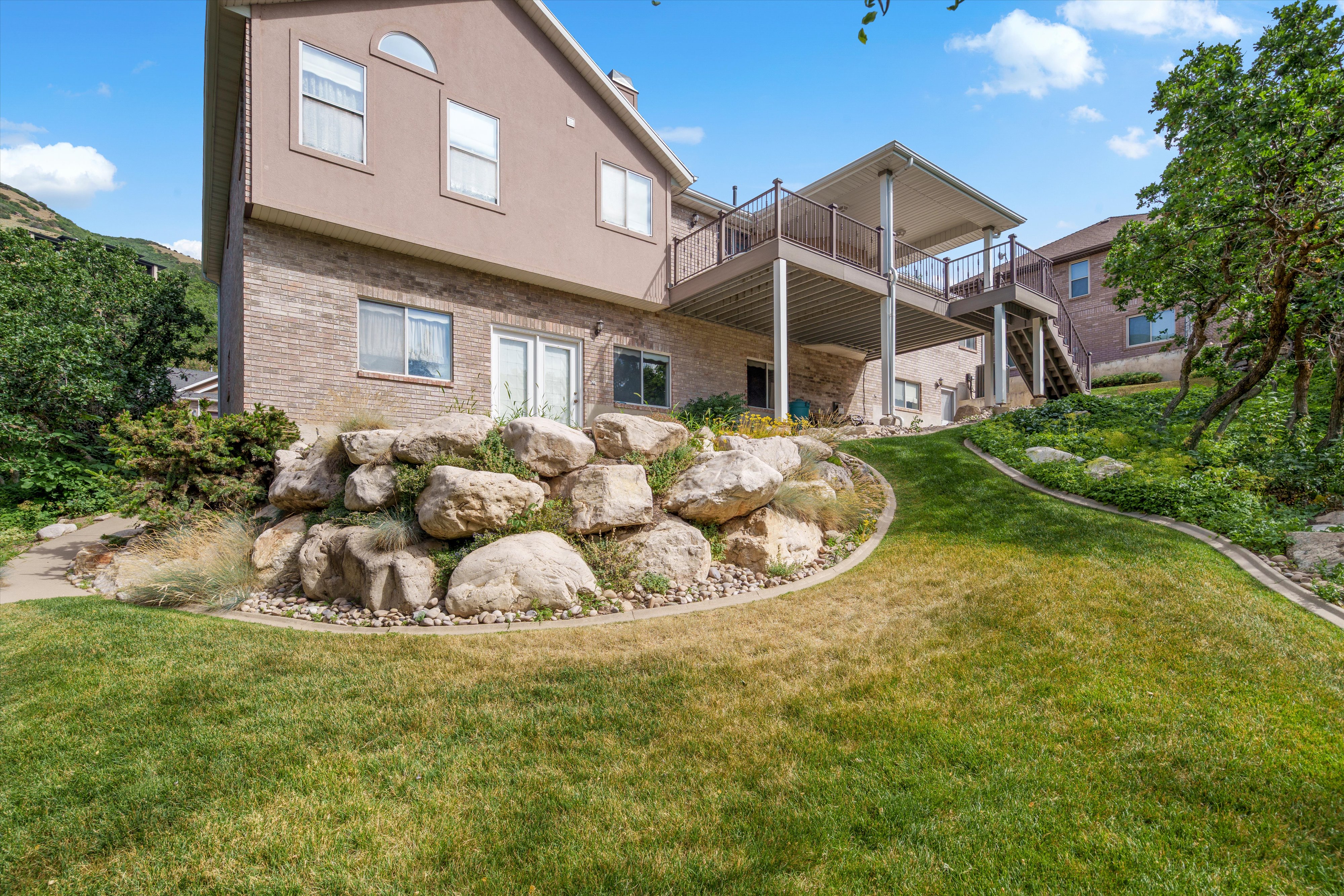 Multi-level deck with covered patio, brick and stucco exterior, and rock retaining wall landscaping
