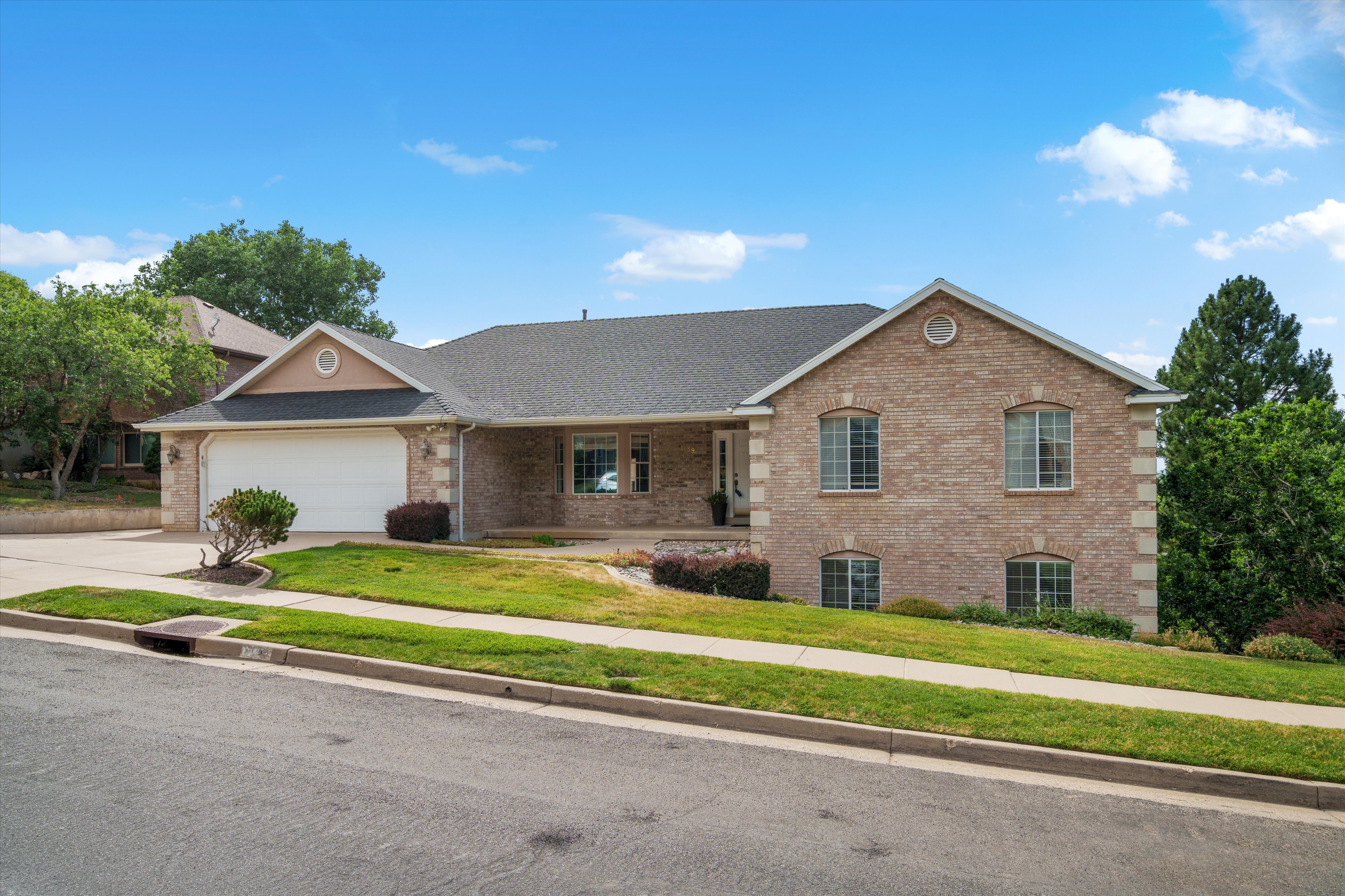 Brick facade residence featuring a two-car garage, pitched shingle roof, arched ground-level windows, and a covered entry porch
