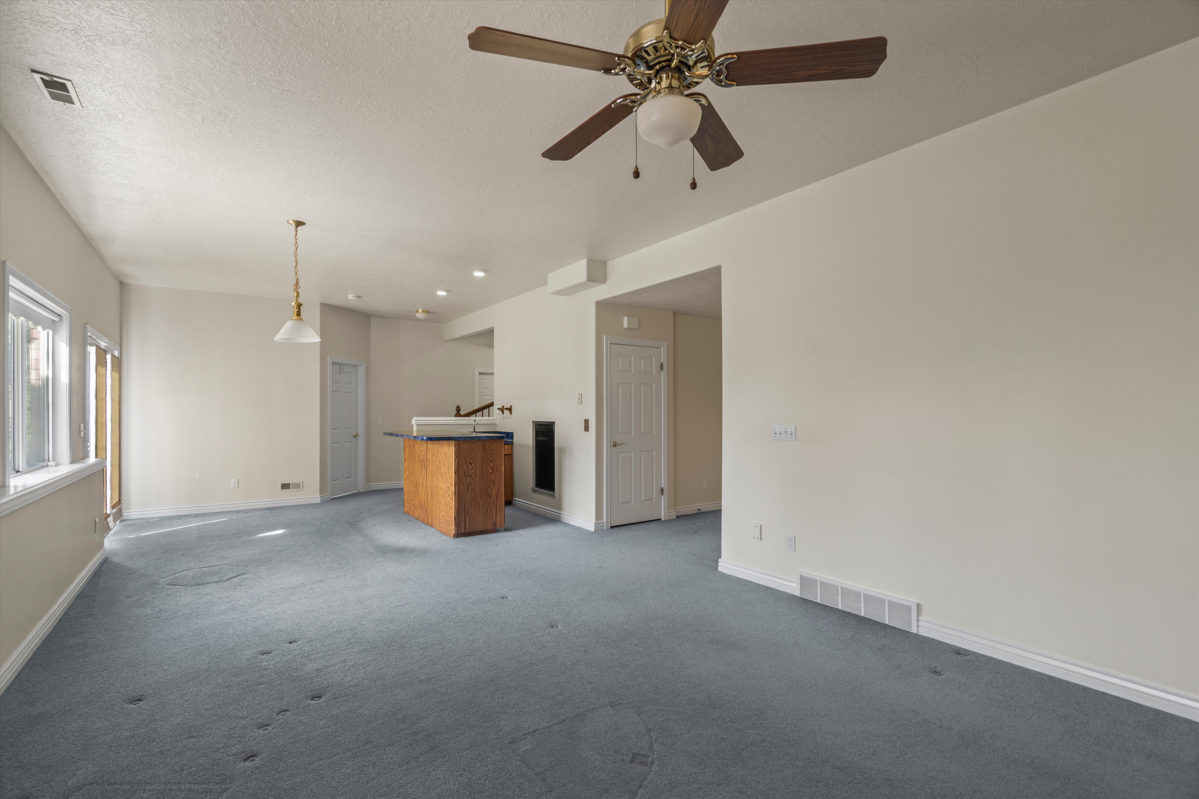 Spacious living area featuring light-toned walls and blue carpeting