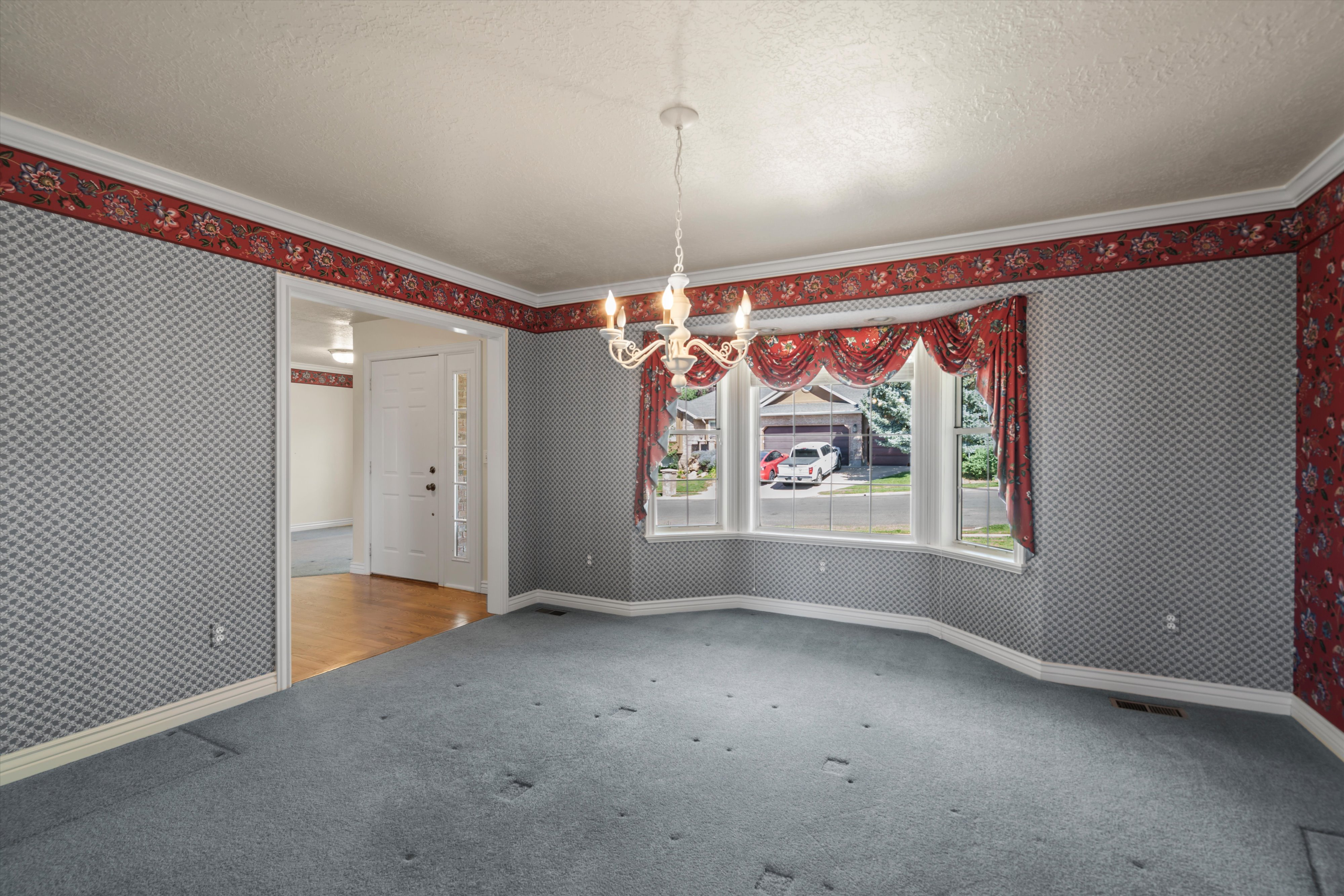 Spacious room featuring a bay window, crown molding, a decorative chandelier, and an open doorway to an entryway with wood-finish flooring