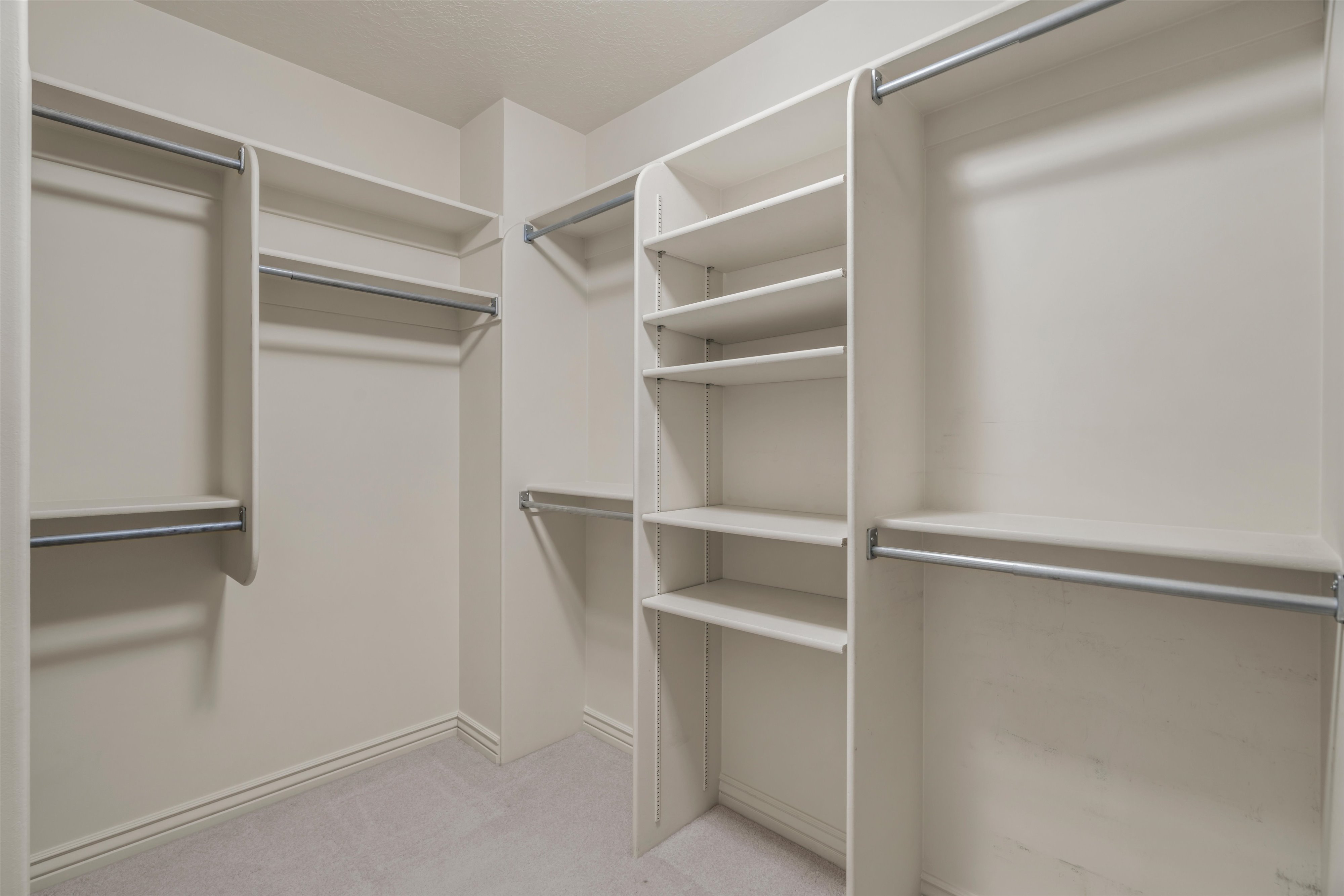 Walk-in closet featuring light beige built-in shelving, multiple hanging rods, and light gray carpeting