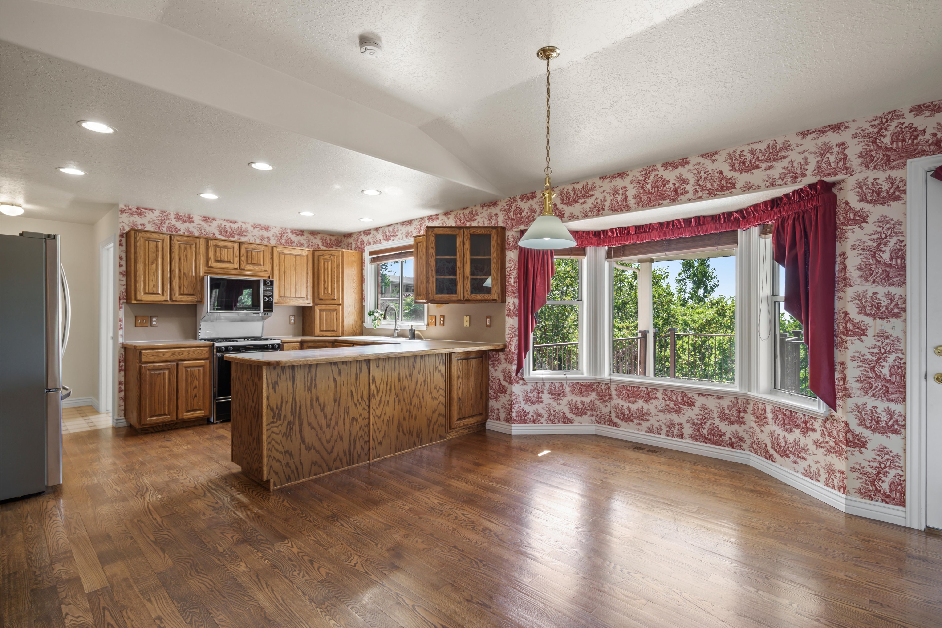 Spacious kitchen and dining area featuring wood-finish flooring, a kitchen island, integrated stainless steel appliances, abundant cabinetry, and a large bay window