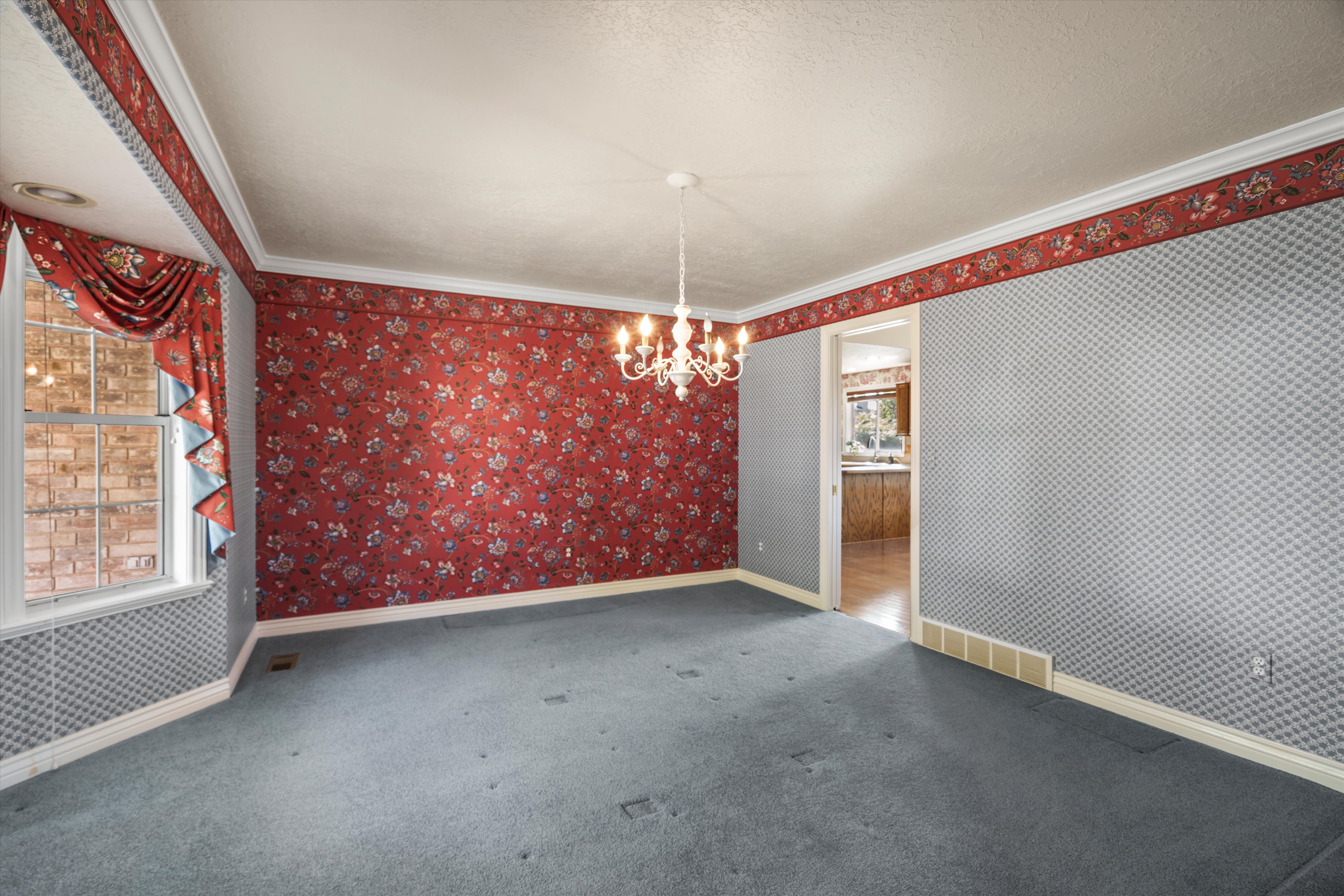 Spacious interior featuring a decorative chandelier, crown molding, and patterned wallpaper