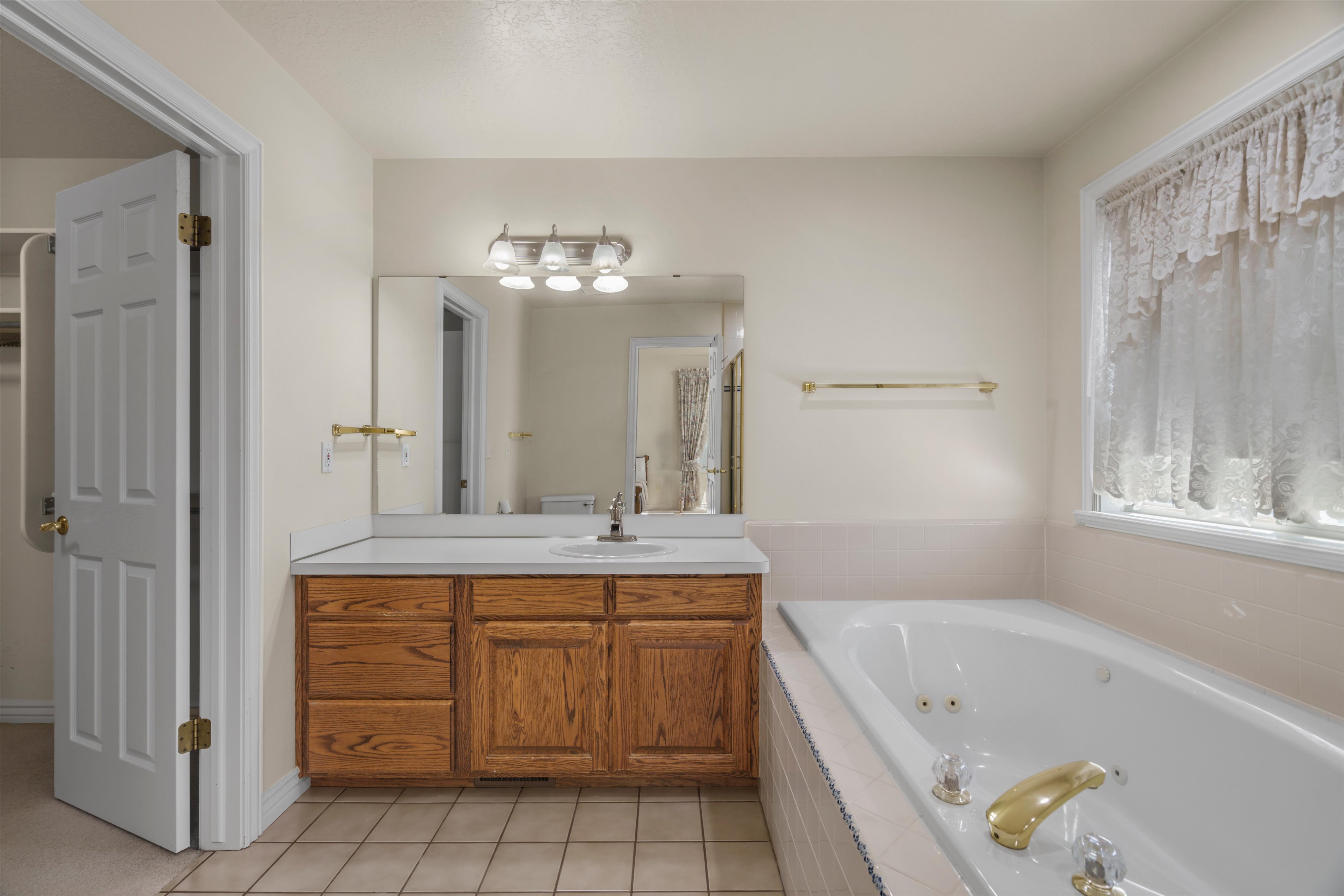 Bathroom featuring a built-in jetted tub, wood-finish vanity with countertop, single sink, and overhead light fixture