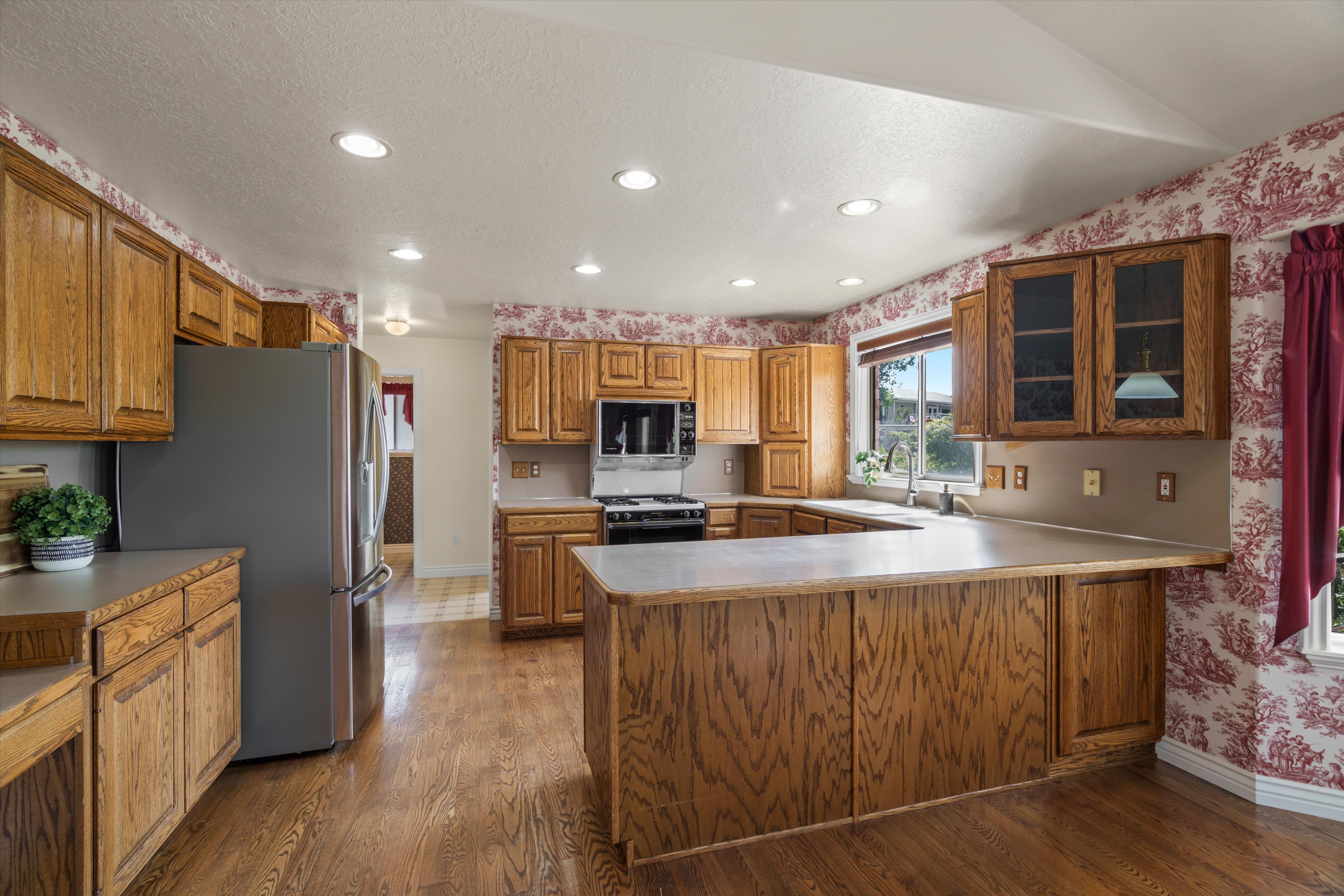 Kitchen featuring wood-finish flooring, wood cabinetry, stainless steel appliances, recessed ceiling lights, and an integrated kitchen island with a countertop extension