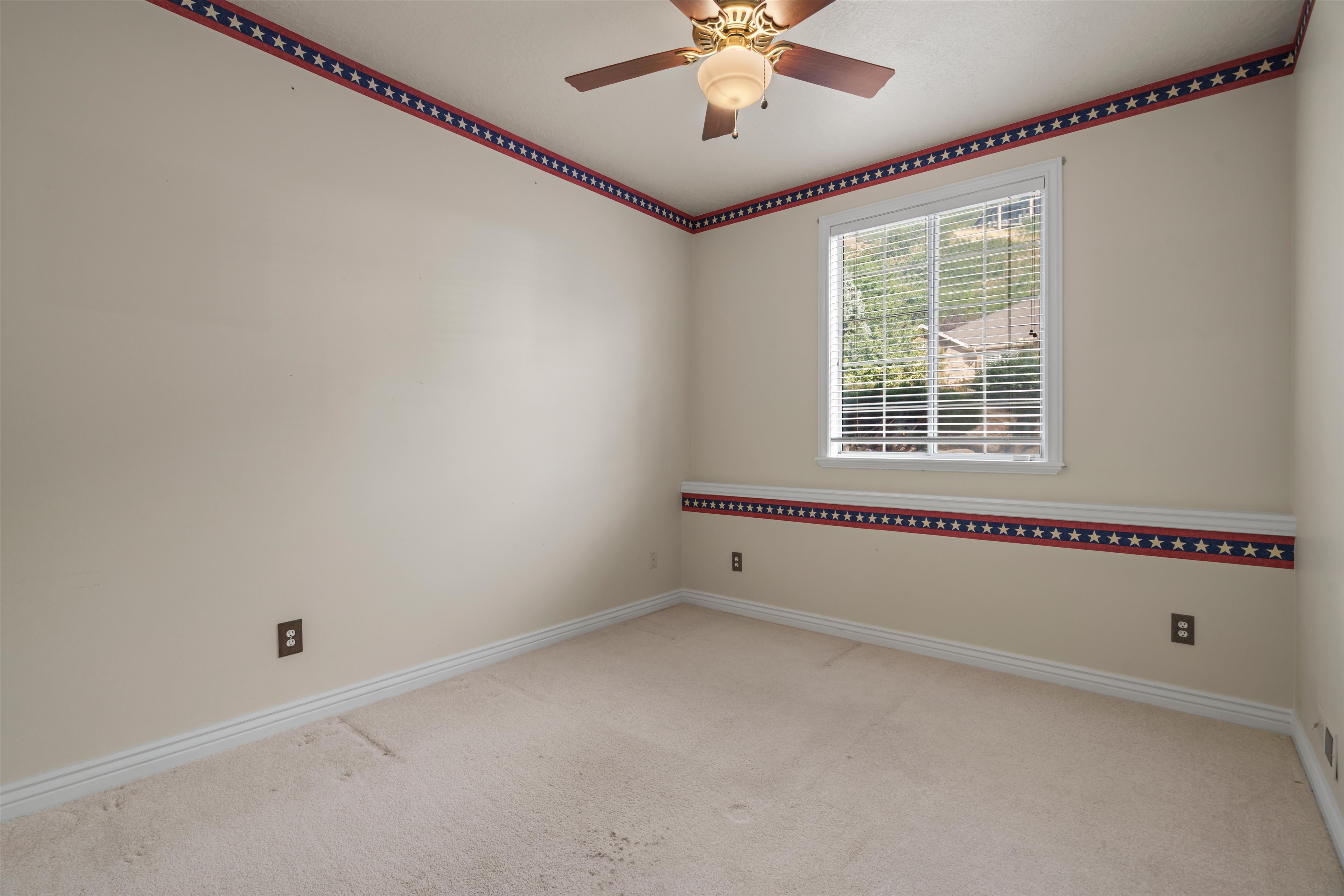 Neutral-toned carpeted room featuring a ceiling fan with integrated lighting, a single window with horizontal blinds, and white baseboards