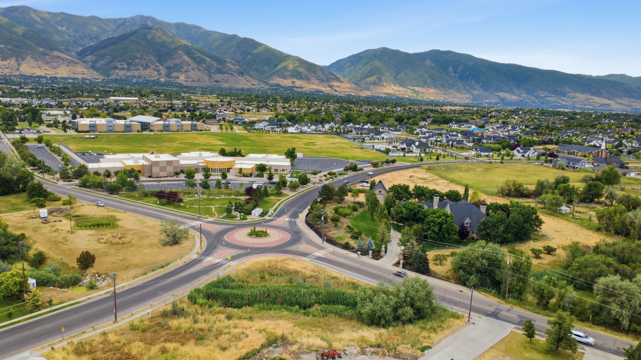 Aerial perspective showcasing a residential area with a prominent roundabout, surrounded by green spaces and distant mountains