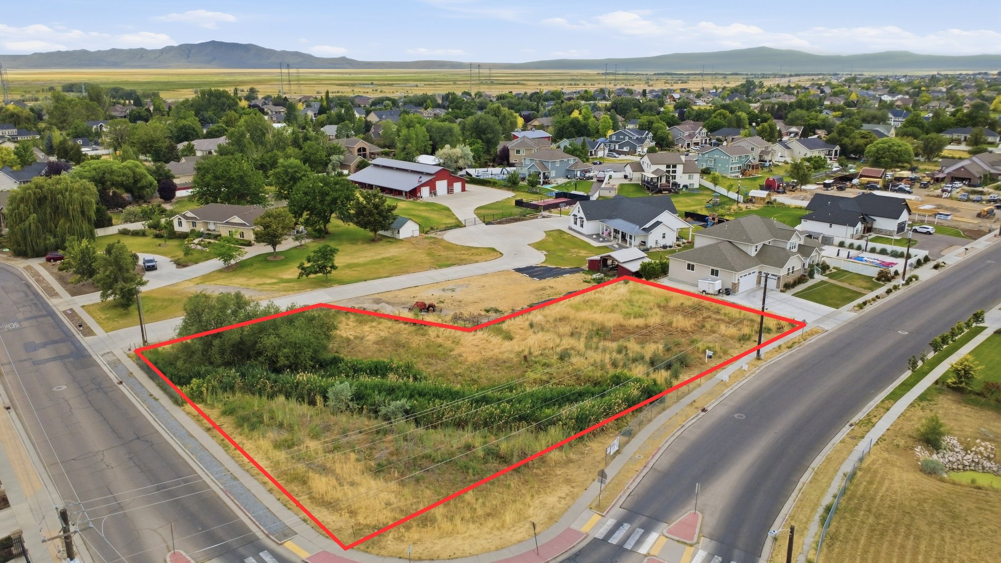 Expansive corner lot featuring a level terrain with natural vegetation, bordered by paved roads