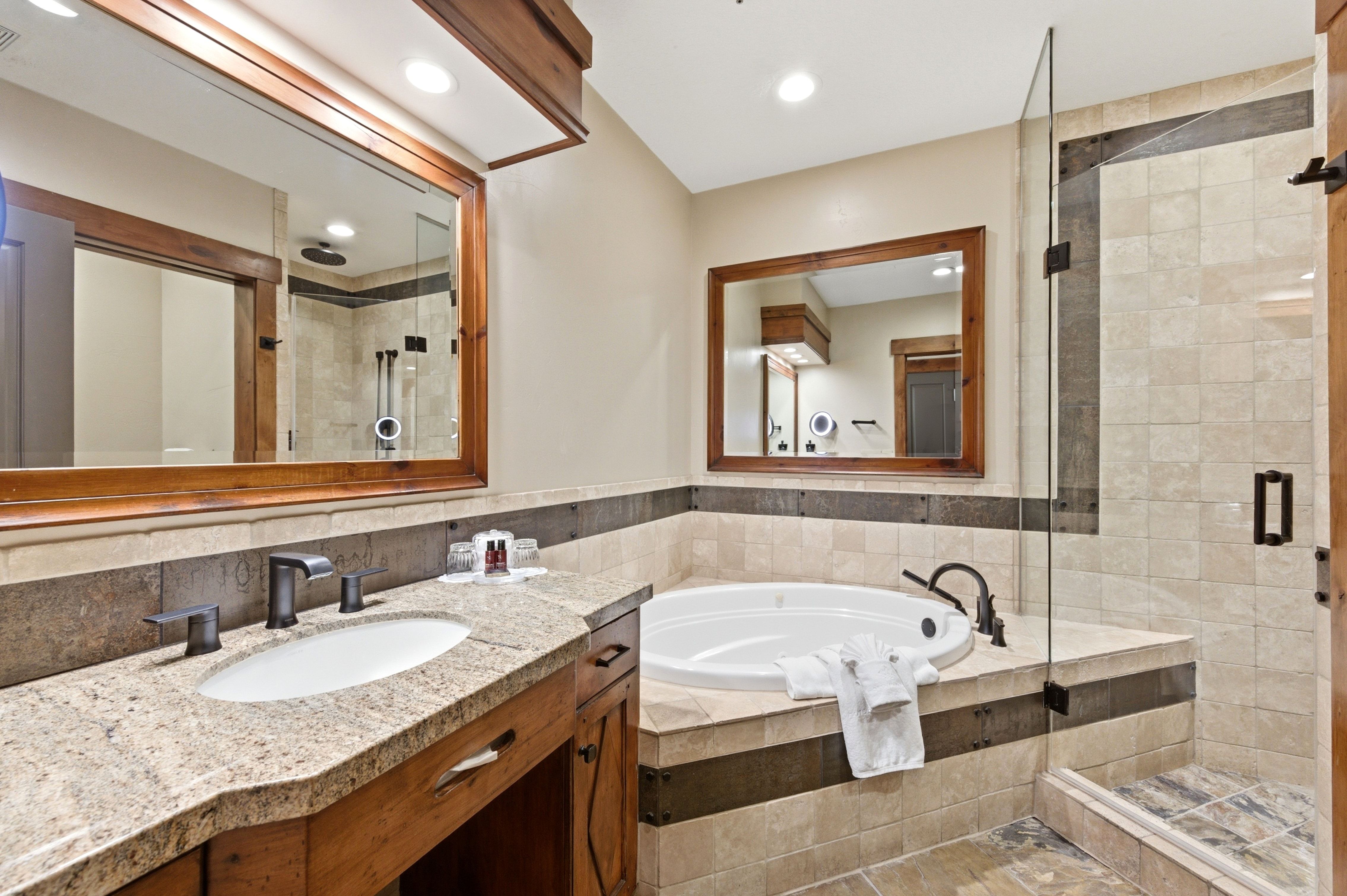Bathroom featuring a built-in jetted tub, a separate glass-enclosed shower, a vanity with a stone-finish countertop, and a wood-framed mirror