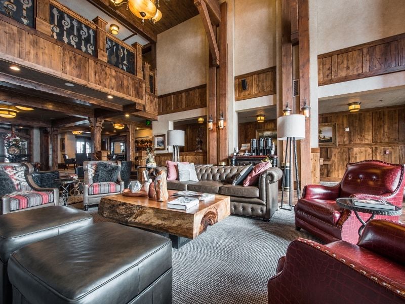 Spacious lounge area featuring rich wood paneling, exposed timber beams, high ceilings, and a large natural wood slab coffee table