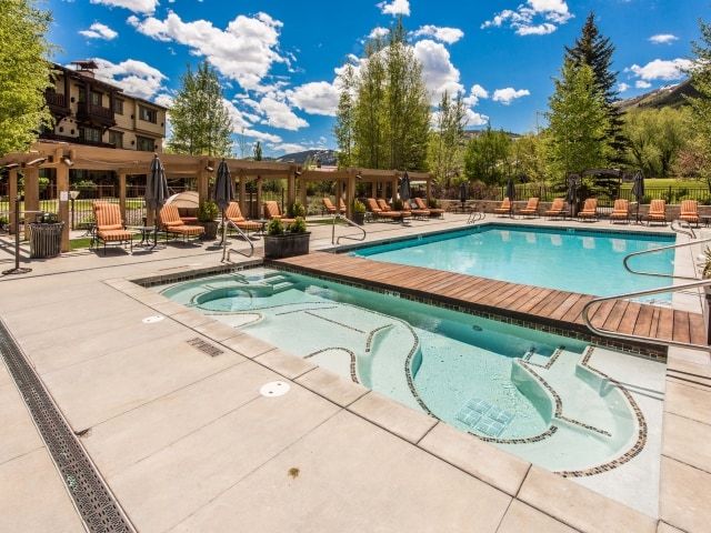 Outdoor aquatic area featuring a rectangular swimming pool, an integrated spa with mosaic tile accents, and a wood-finish bridge
