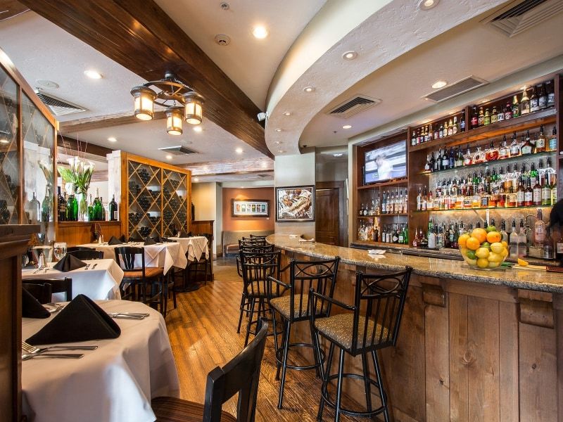 Interior bar and dining area featuring wood-finish flooring, a stone-top bar, built-in shelving, a recessed flat-screen display, and a wood-slat wine storage wall