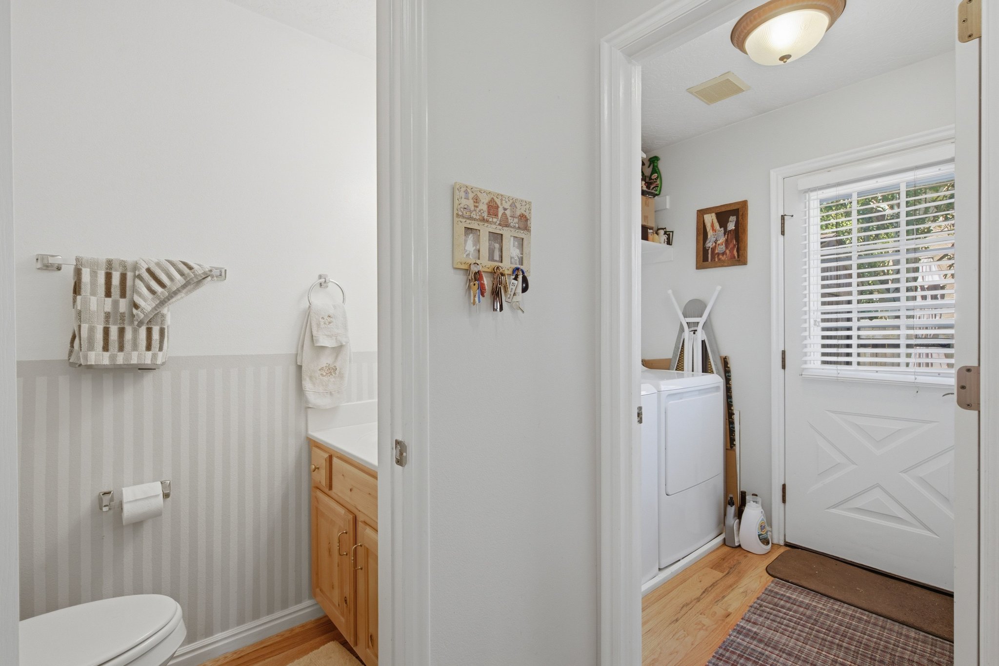 Utility area featuring a white paneled door with horizontal blinds, wood-finish flooring, and a flush mount light fixture